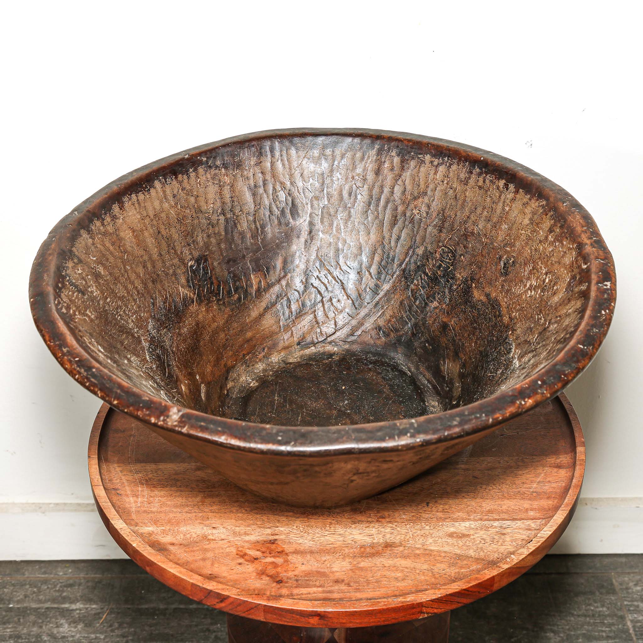 Vintage round brown wooden bowl from Ethiopia on a wooden stand against a white background