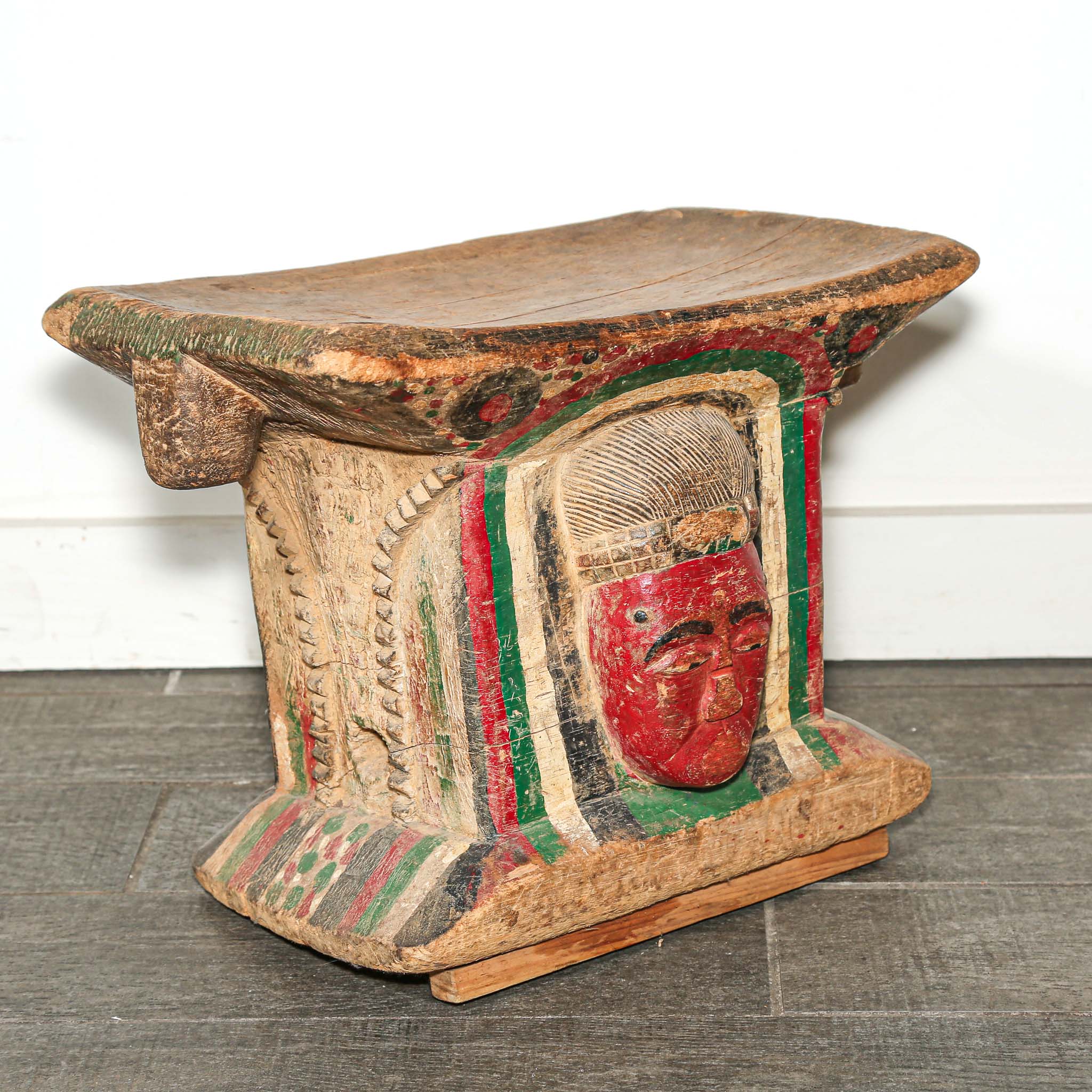 Wooden African stool with a red face design on a white background