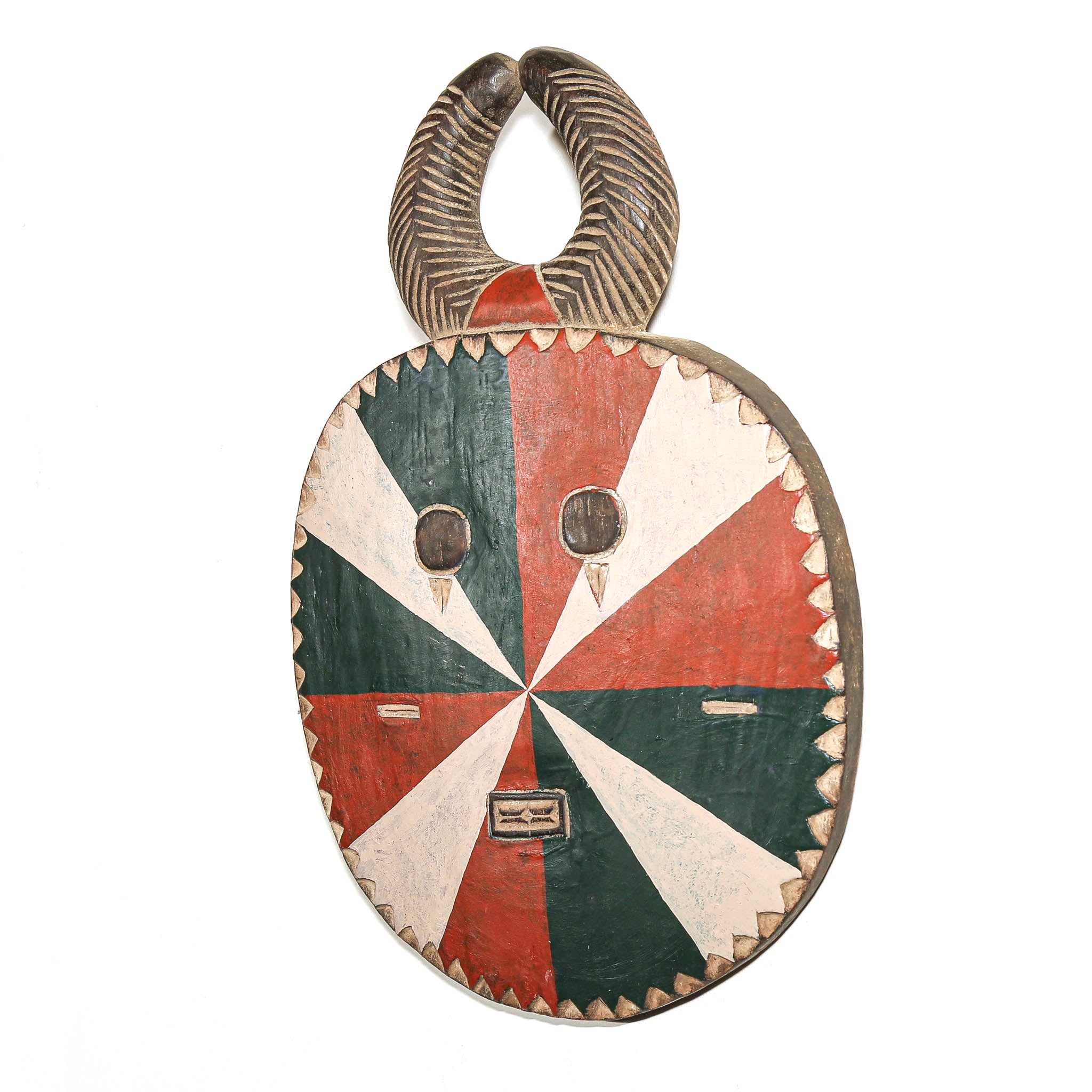 A hand-carved African wooden mask with a horn-like top handle, featuring a painted starburst design in red, green, and off-white, with two circular eye cutouts and a small rectangular mouth area.