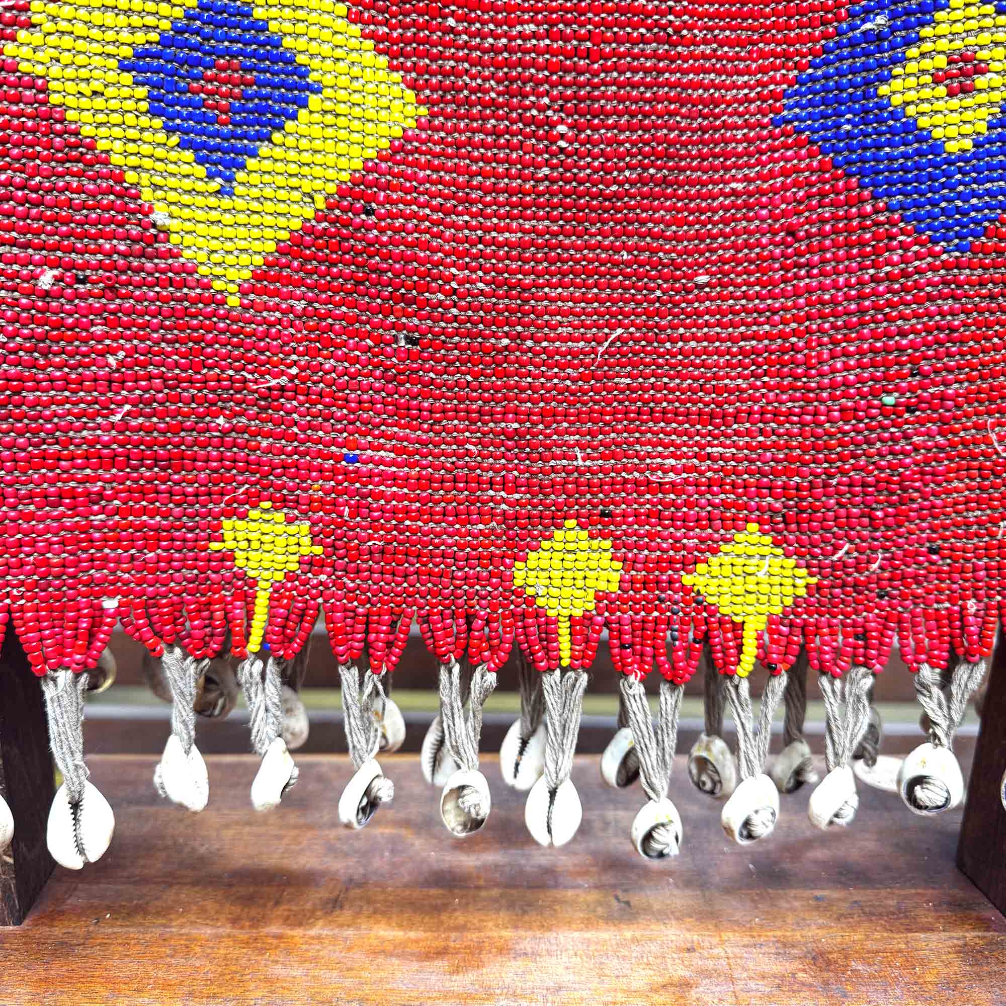 Close-up of a red beaded african style shirt with yellow floral patterns on a wooden surface