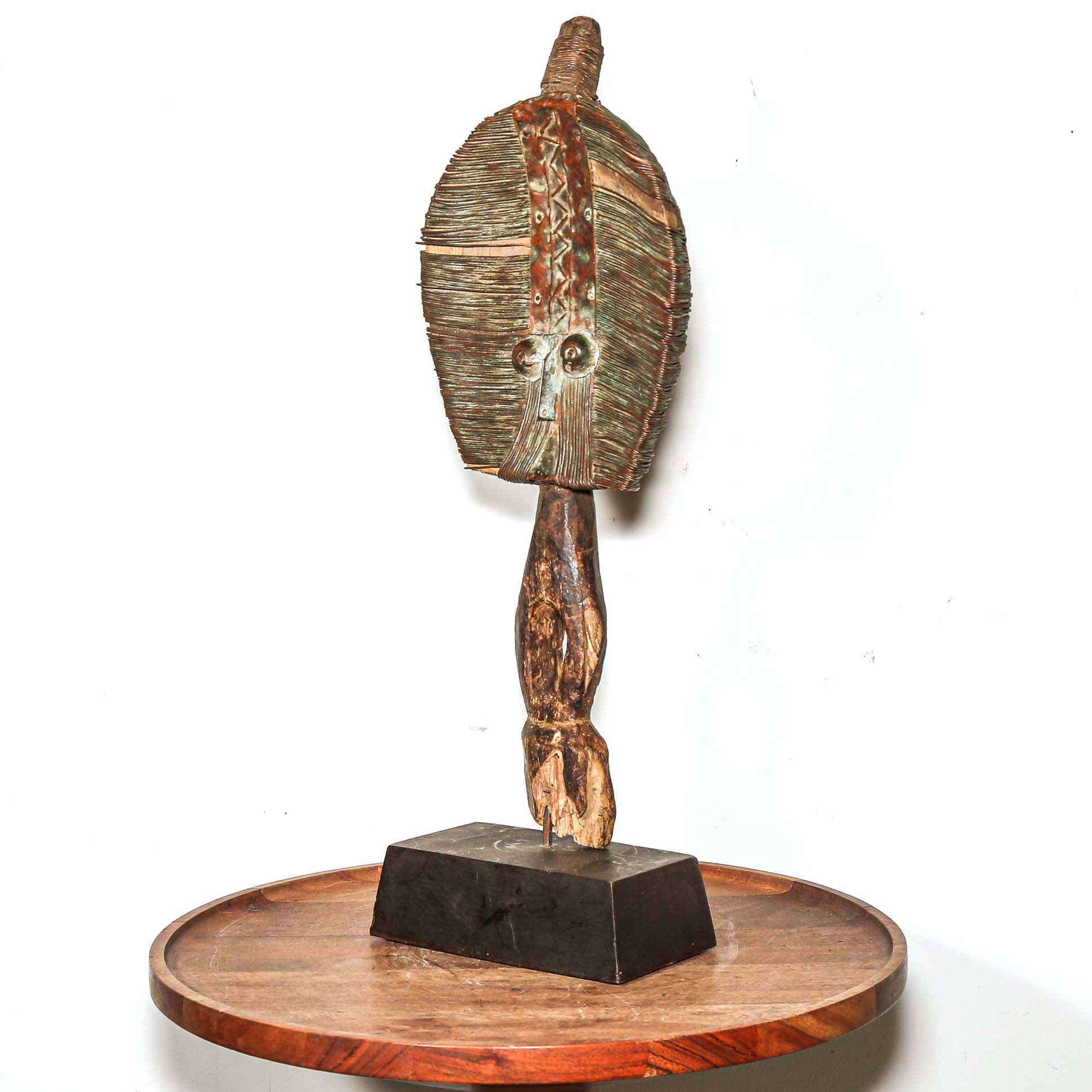 Wooden protective traditional mask from Gabon made from wood and metal on a round wooden table with a white background 3/4 view
