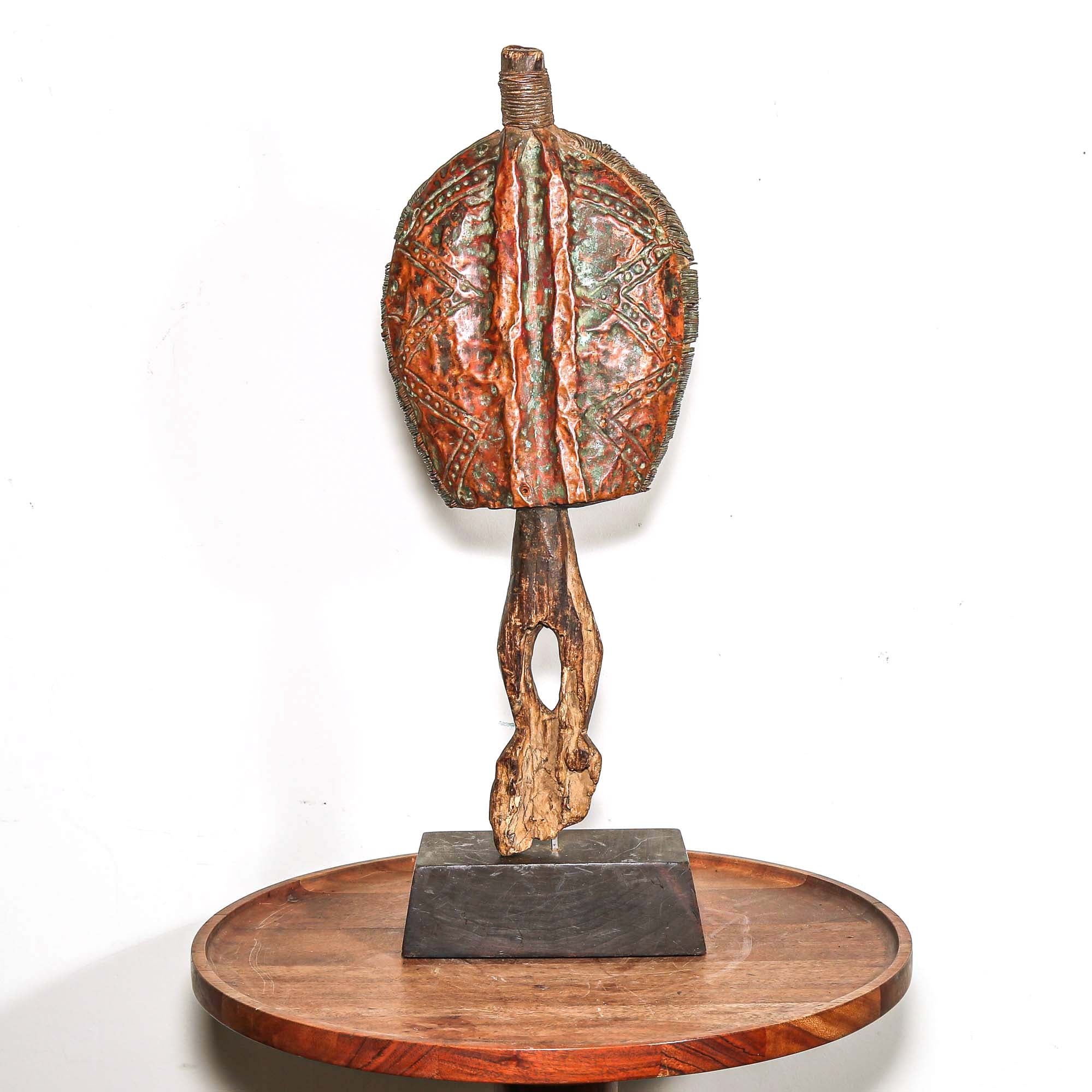 Wooden protective traditional mask from Gabon made from wood and metal on a round wooden table with a white background shown from behind