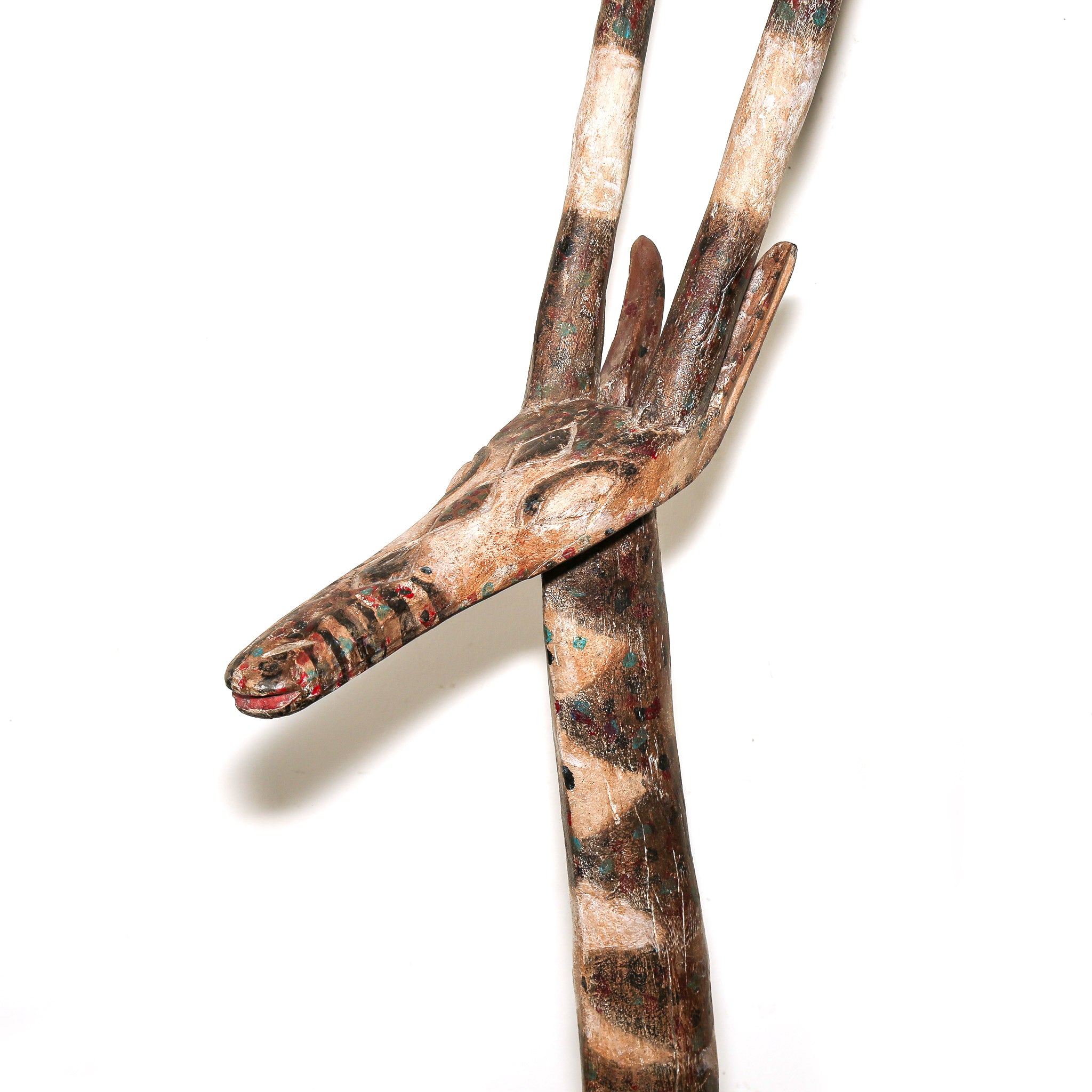 A hand-carved wooden sculpture of a antelope featuring natural wood grain, dark markings, and small red and green painted accents, set against a plain white background.