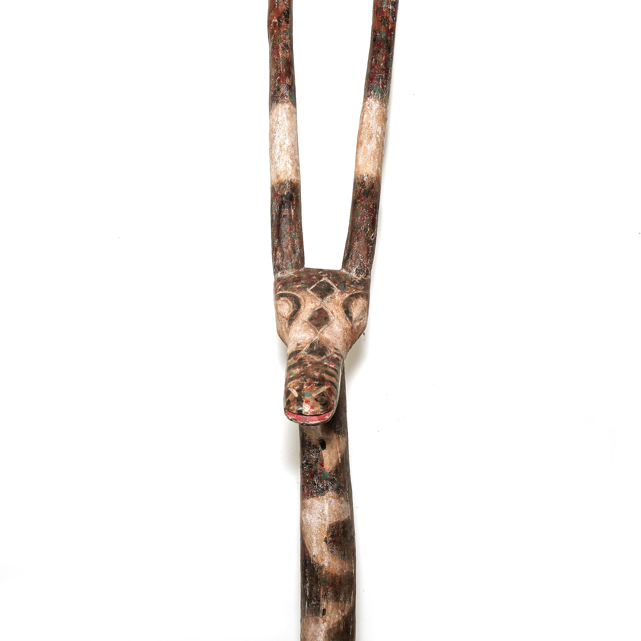 A hand-carved wooden tribal sculpture of a antelope head with long curved horns, featuring natural wood grain and small red painted accents on the mouth and forehead, set against a plain white background.