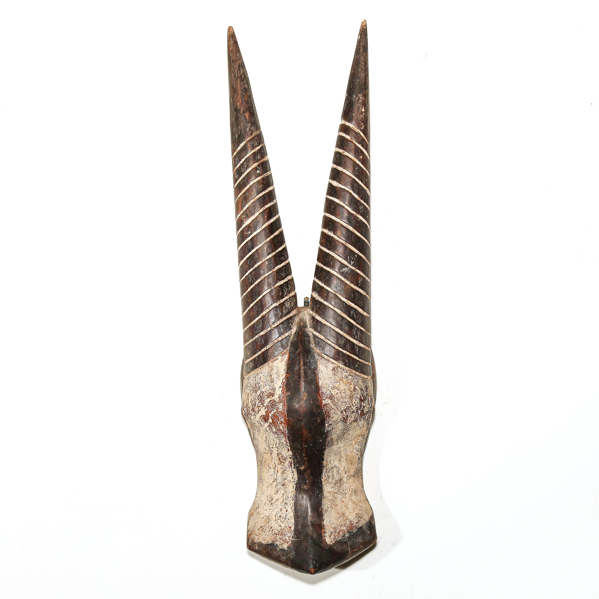 A carved horned decorative object, likely a mask head or sculptural decor, featuring two long pointed horns with spiral carved details and a textured, weathered finish on a plain white background.