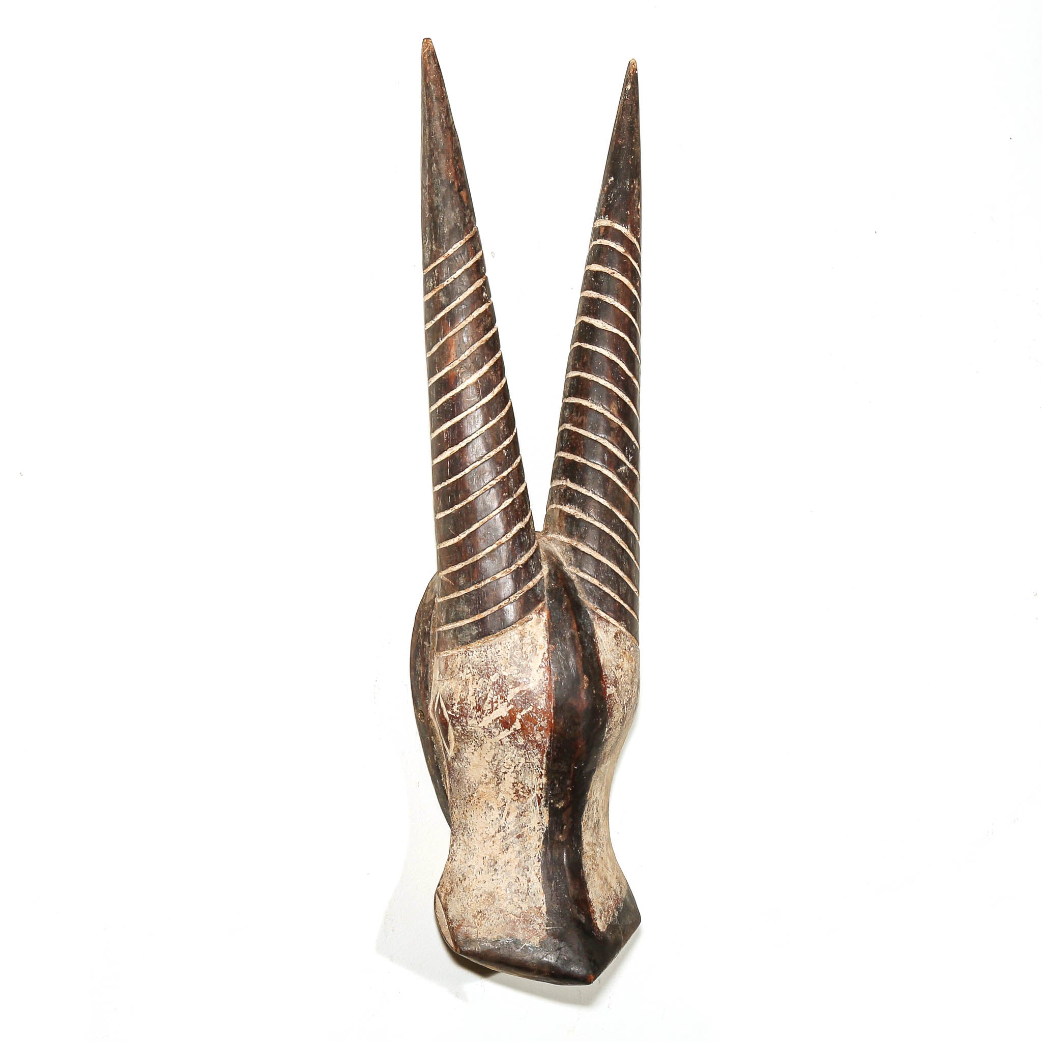 A carved wooden decorative object with two long pointed horns, featuring dark brown and beige wood tones with carved horizontal lines, set against a plain white background.