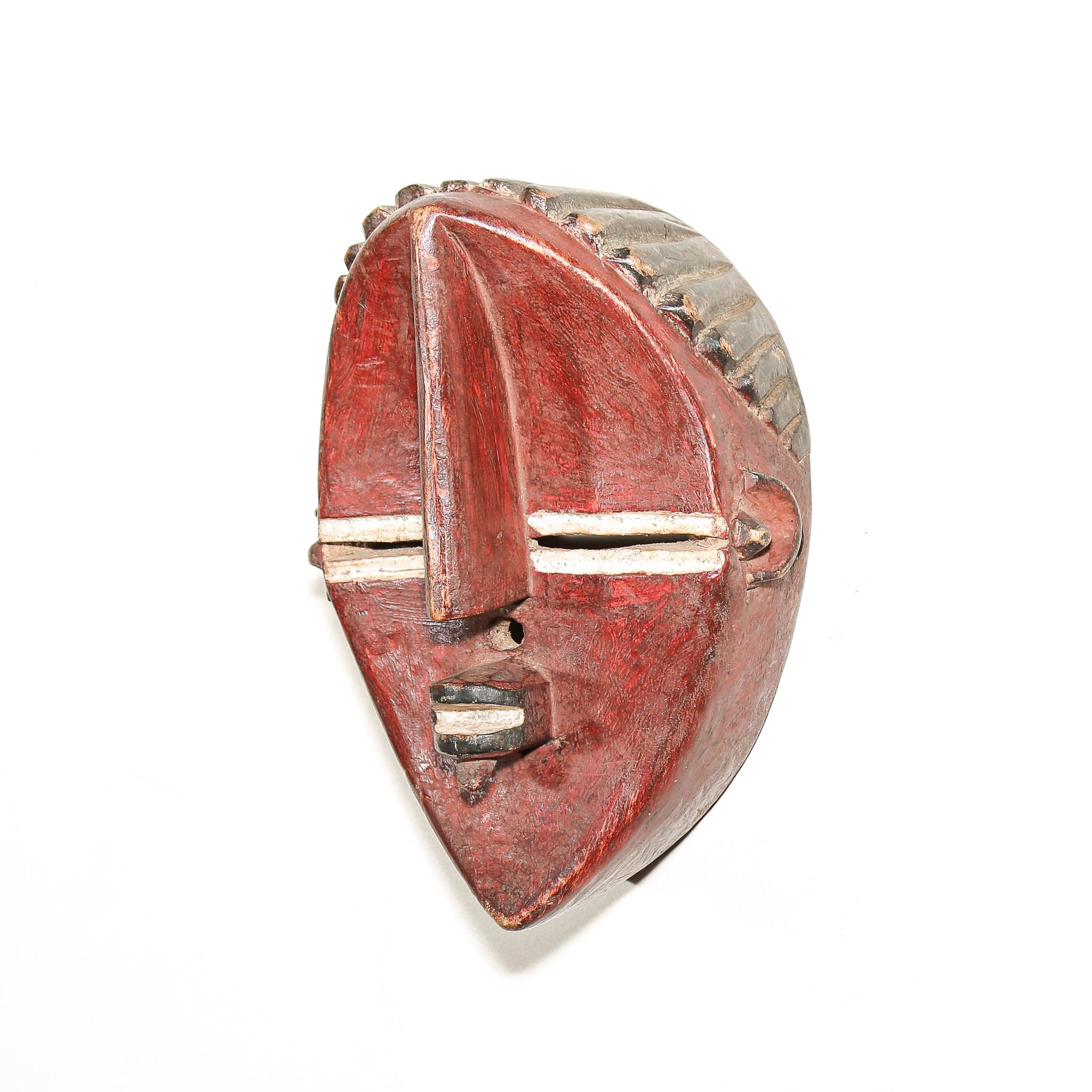 A carved wooden mask with a weathered red-painted face, featuring a textured gray and brown pattern on the top, photographed against a plain white background.