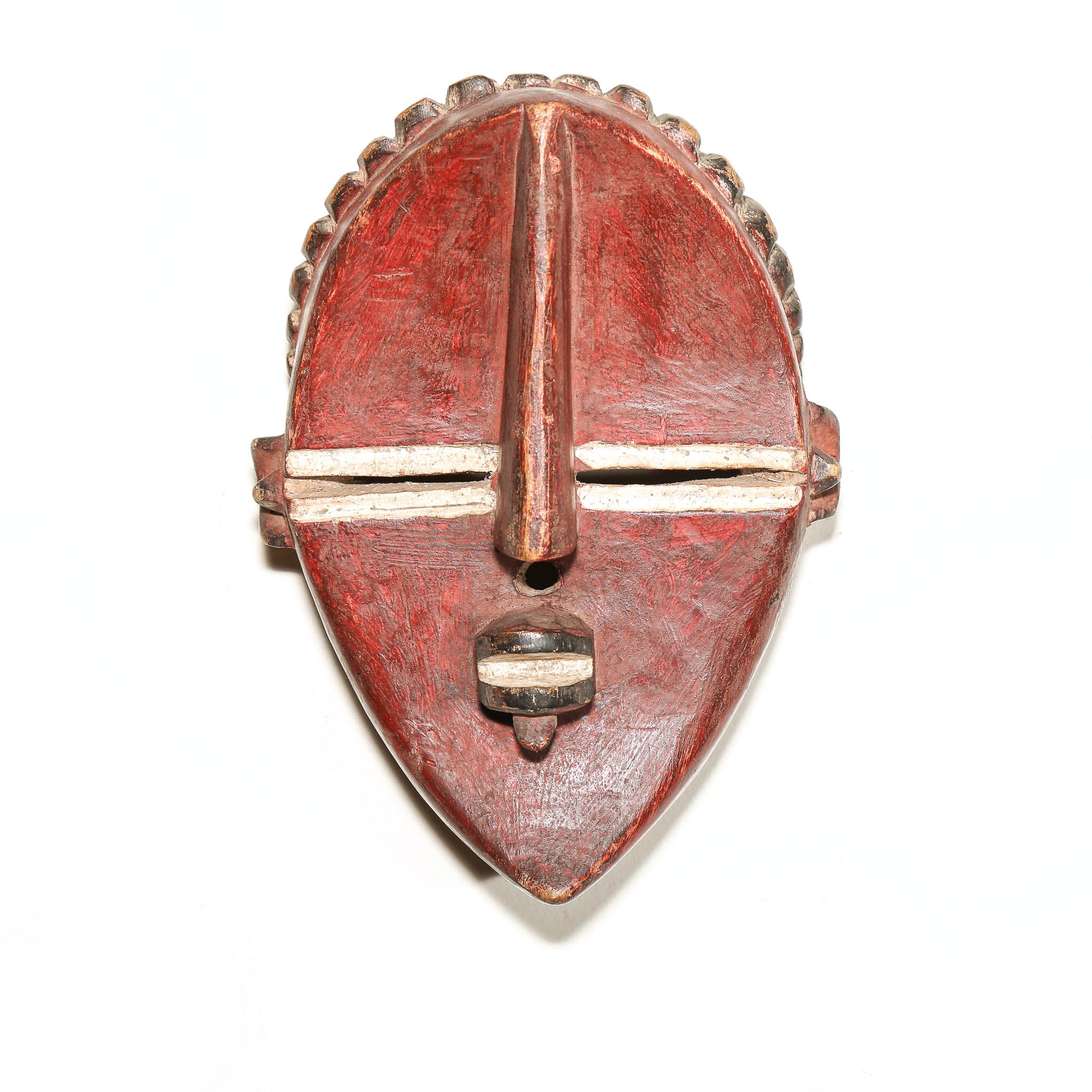 A carved wooden African-style mask or decorative plaque in reddish-brown tones with white painted accents, photographed against a plain white background.