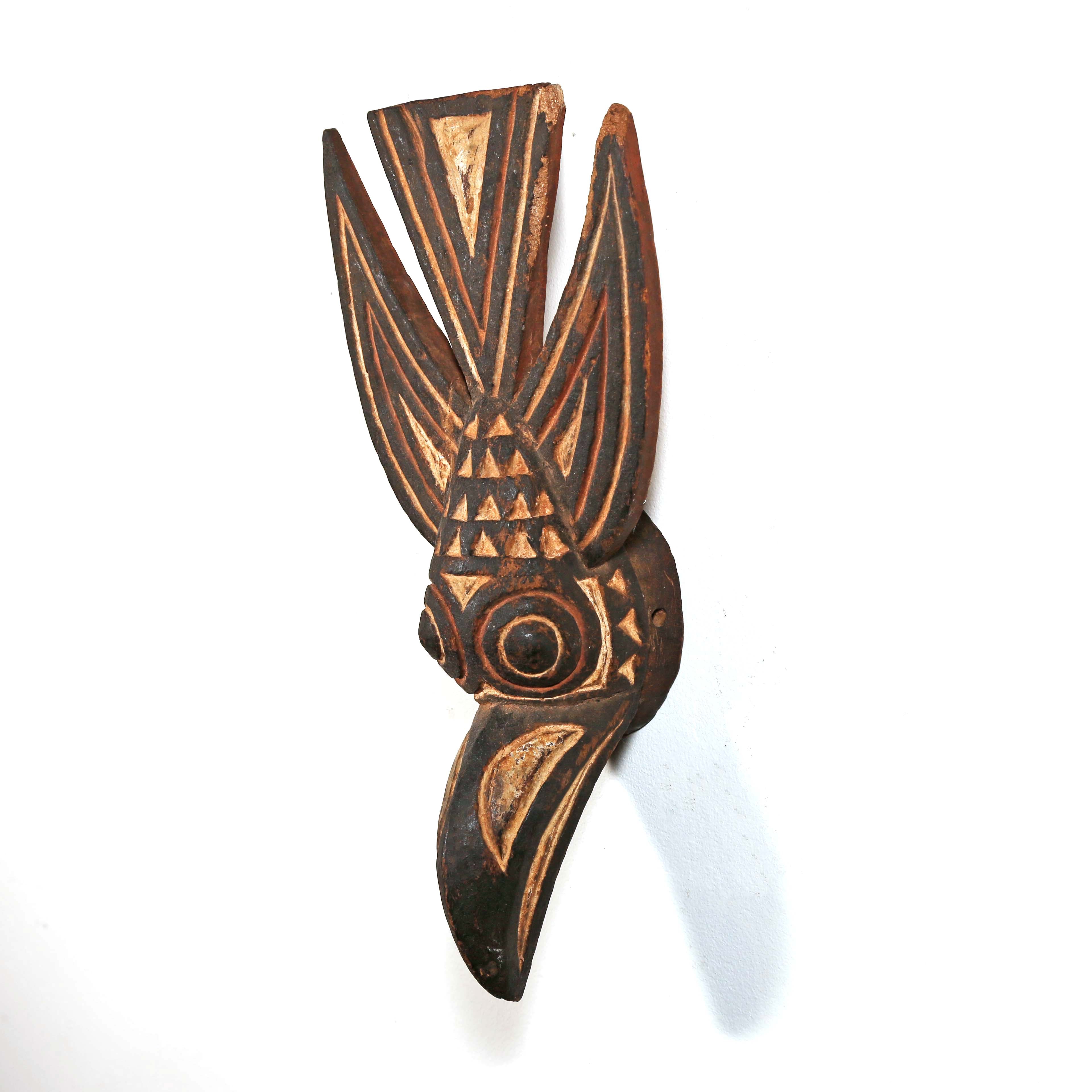Decorative wooden wall hanging with tribal patterns in the shape of a bird from Africa on a white background