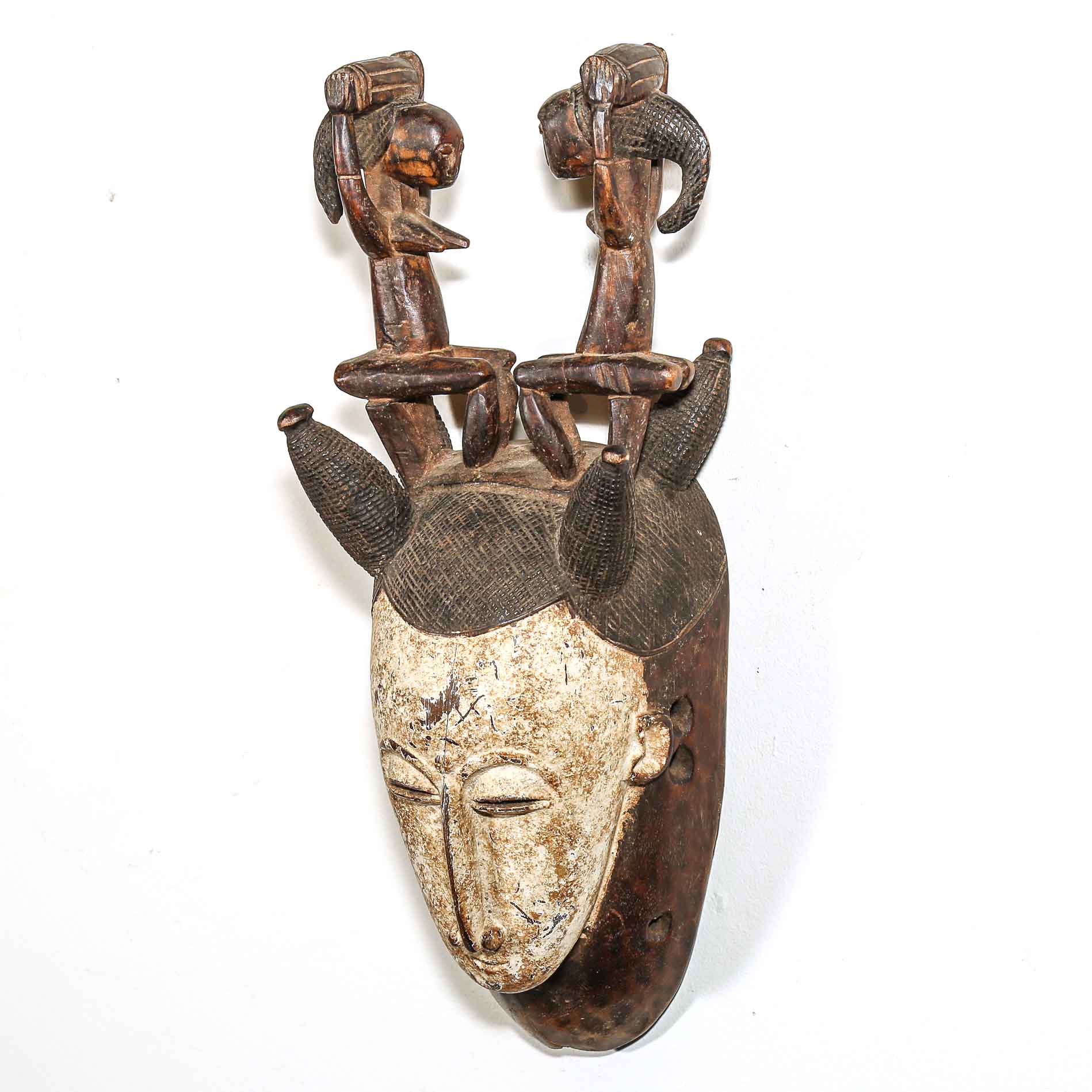 African wooden mask with intricate carvings and a white face on a white background