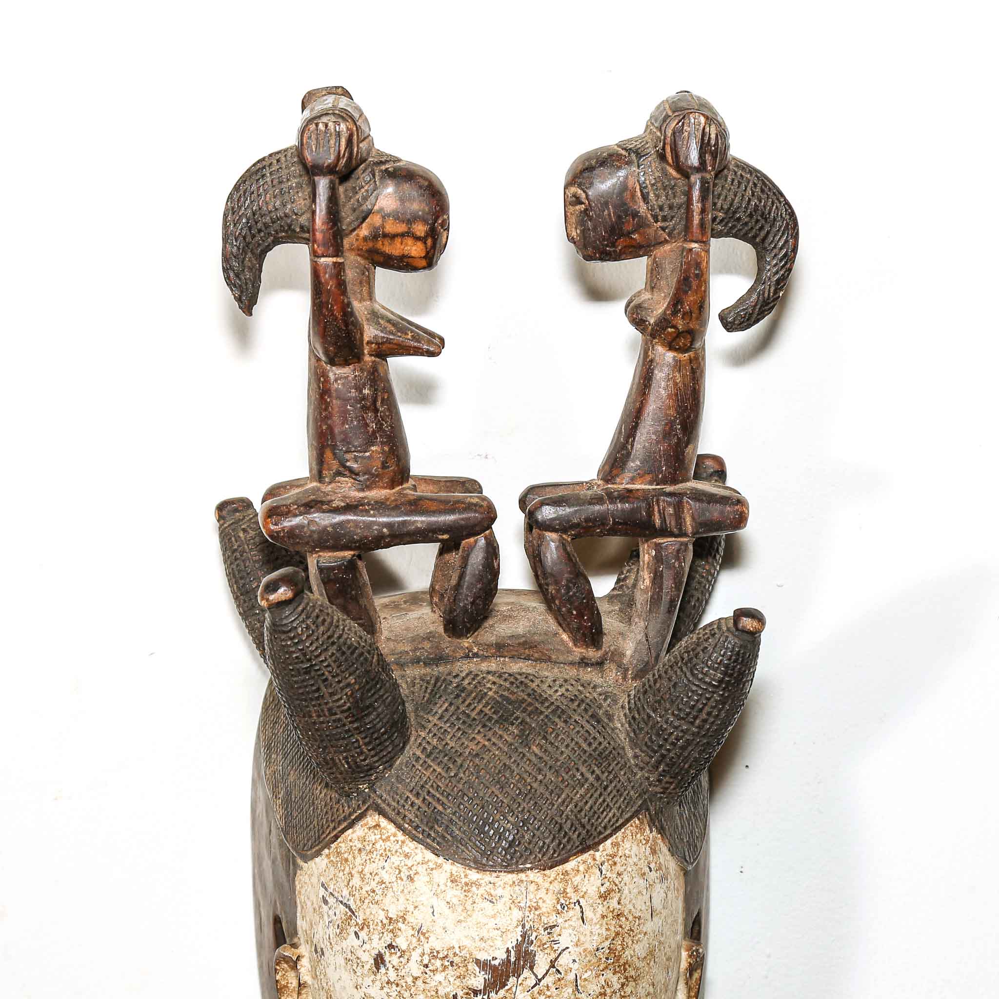 two sitting figures carved on top of a wooden mask from Africa on a white wall