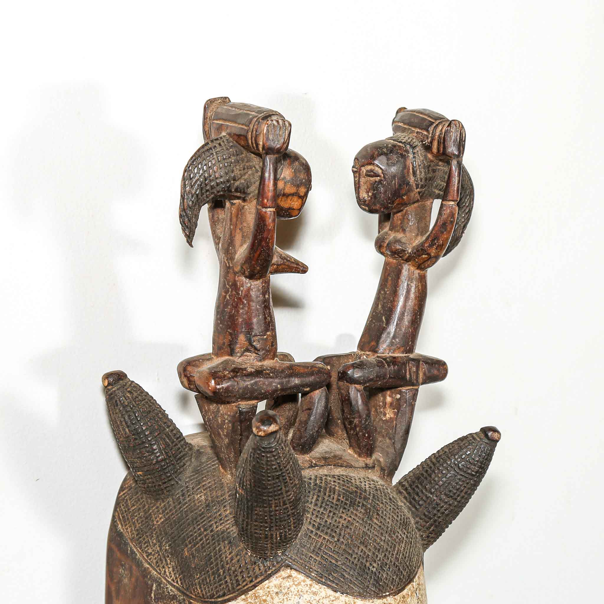 Wooden sculpture of two figures with a third figure on top, on a white background