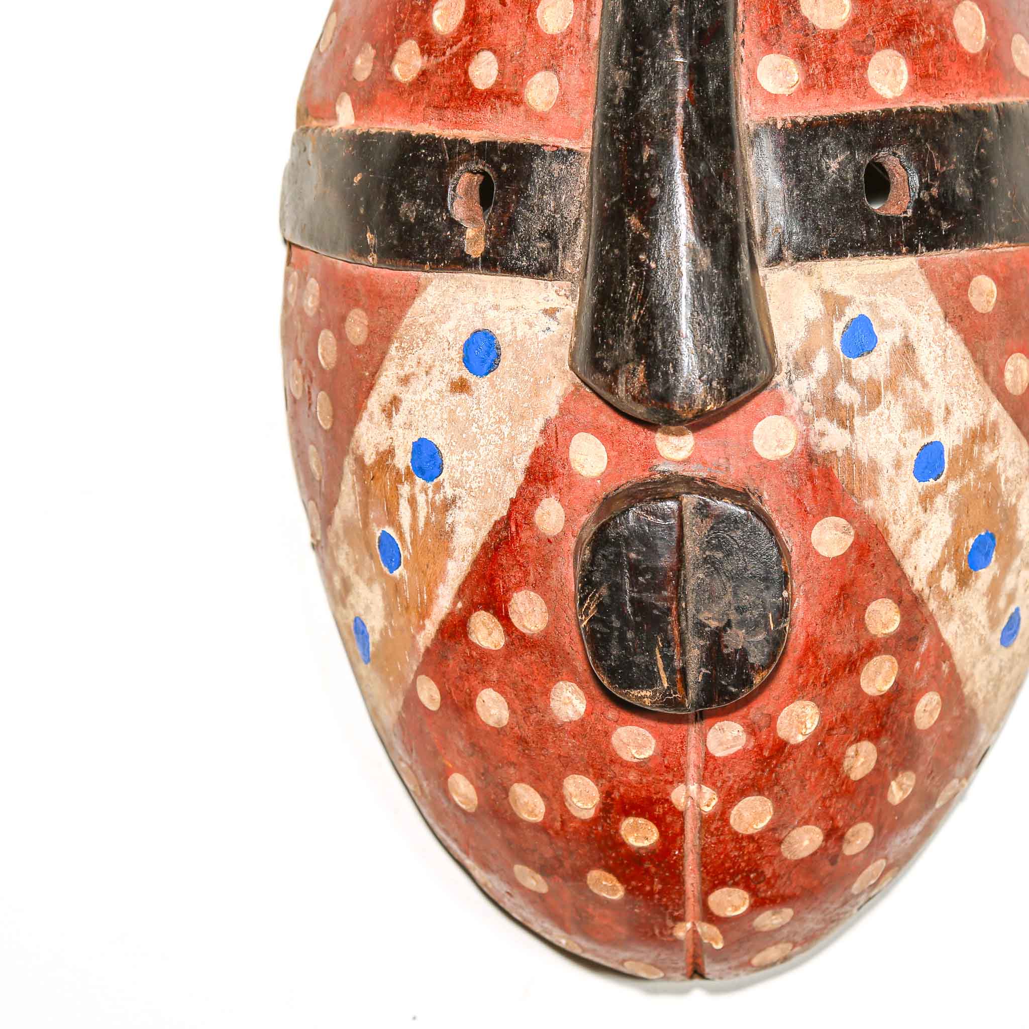 Close-up of a decorative carved wood mask with red, black, and blue patterns on a white background from Africa