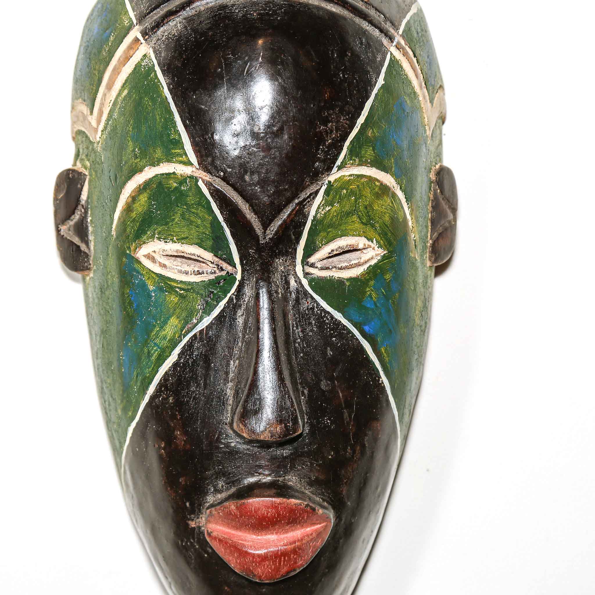 Close up of a African decorative mask with green, black, and red colors on a white background with black art details