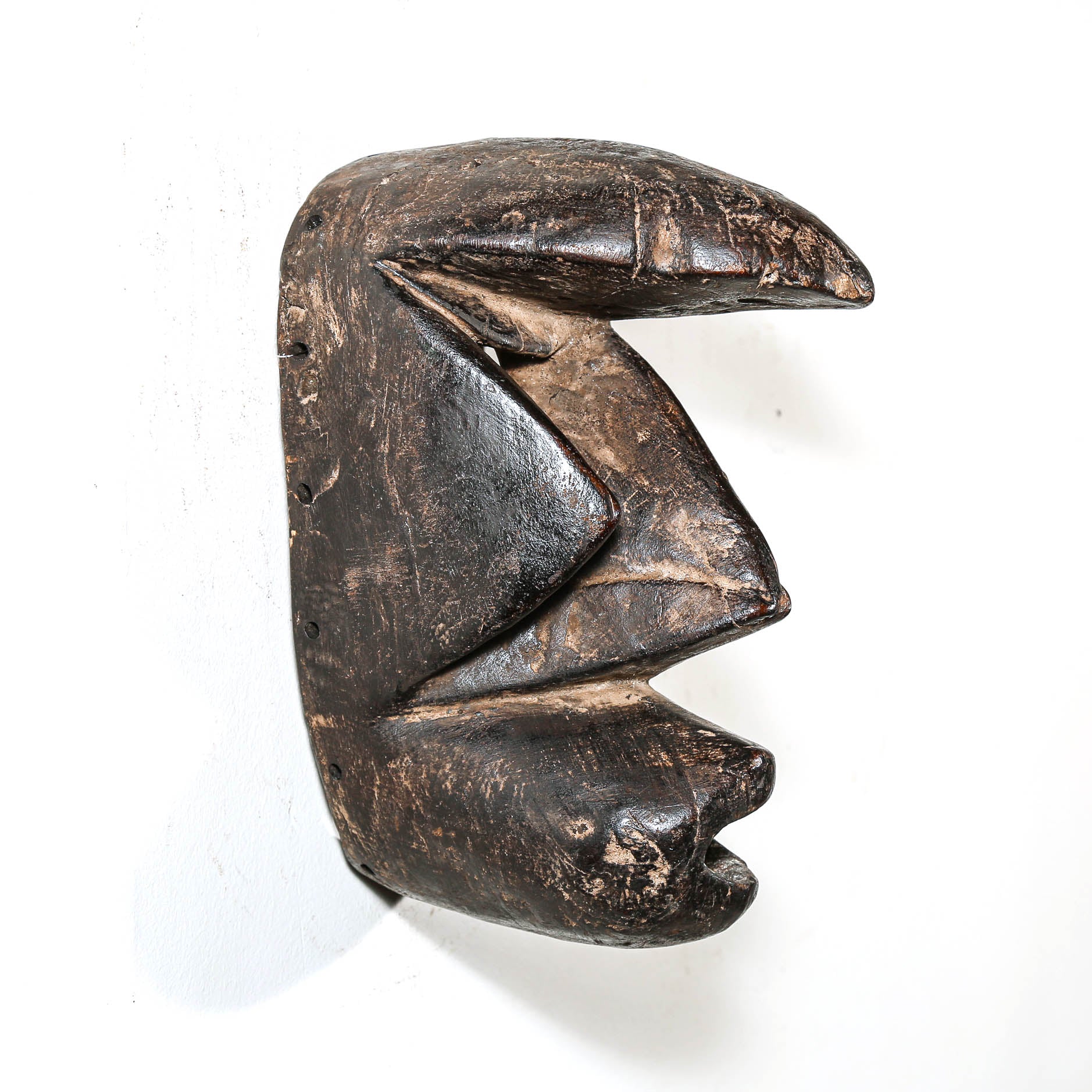 Carved antique tribal ceremonial black wooden mask on a white background