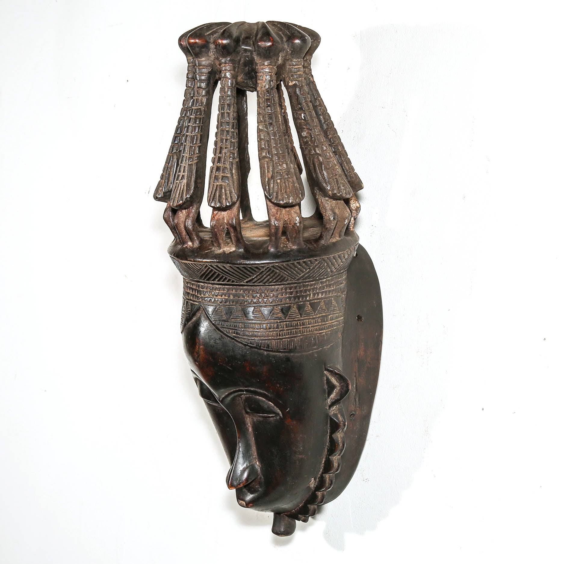 finely carved African mask with bird headdress on a white wall