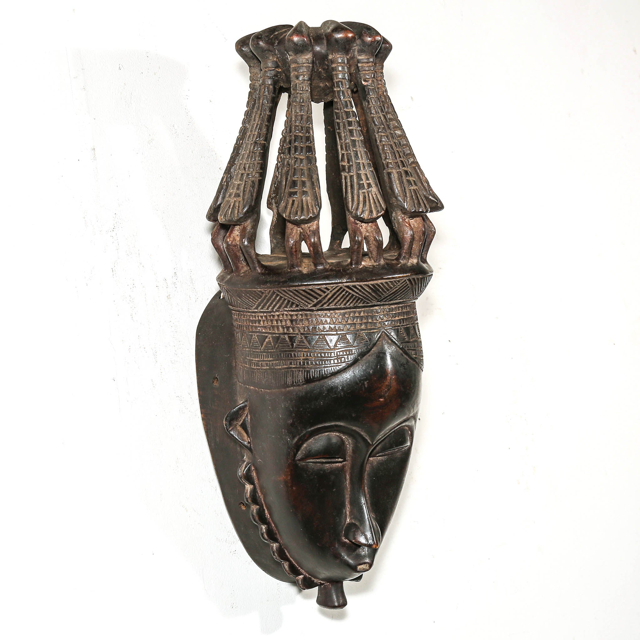 African mask with intricate bird headdress on a white wall