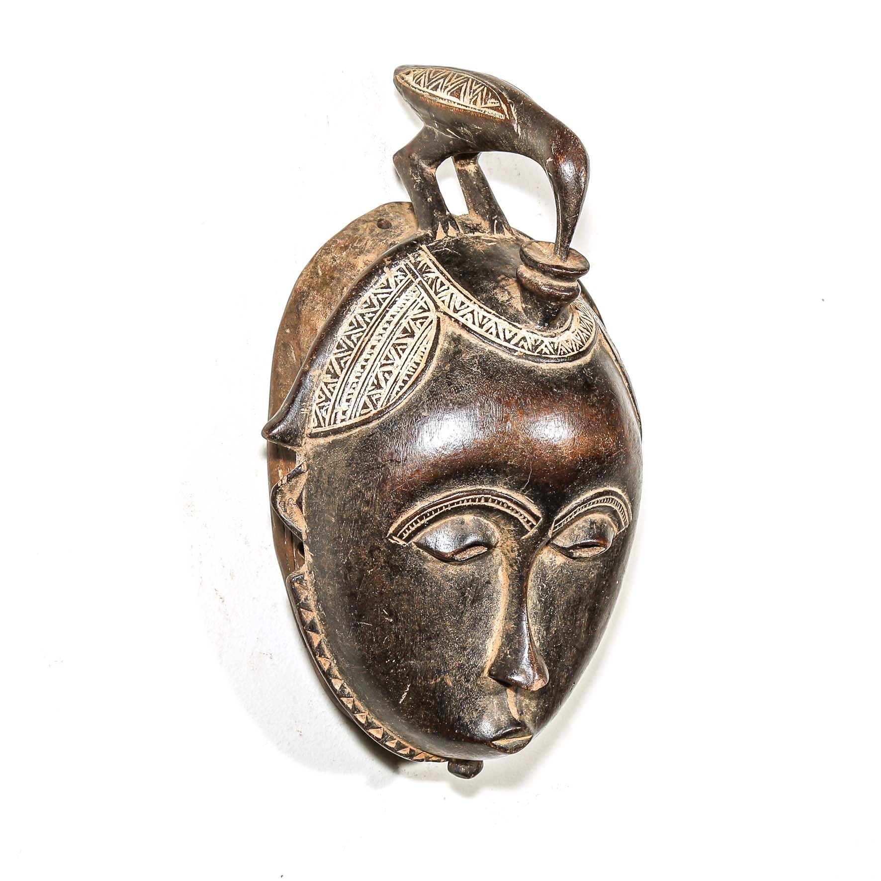 Bronze mask with intricate hand carved African designs on a white background