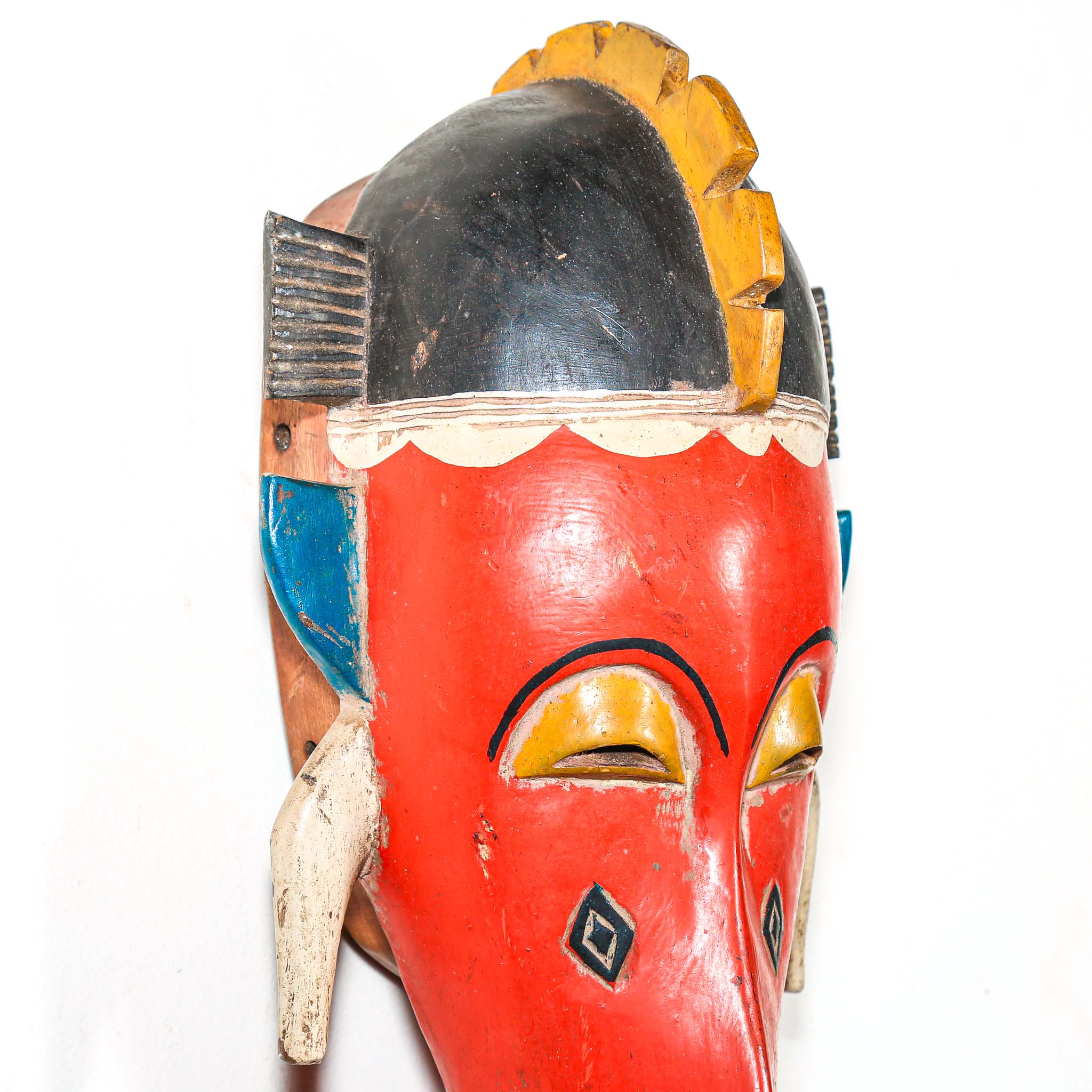Colorful wooden mask with red face and yellow accents on a white background
