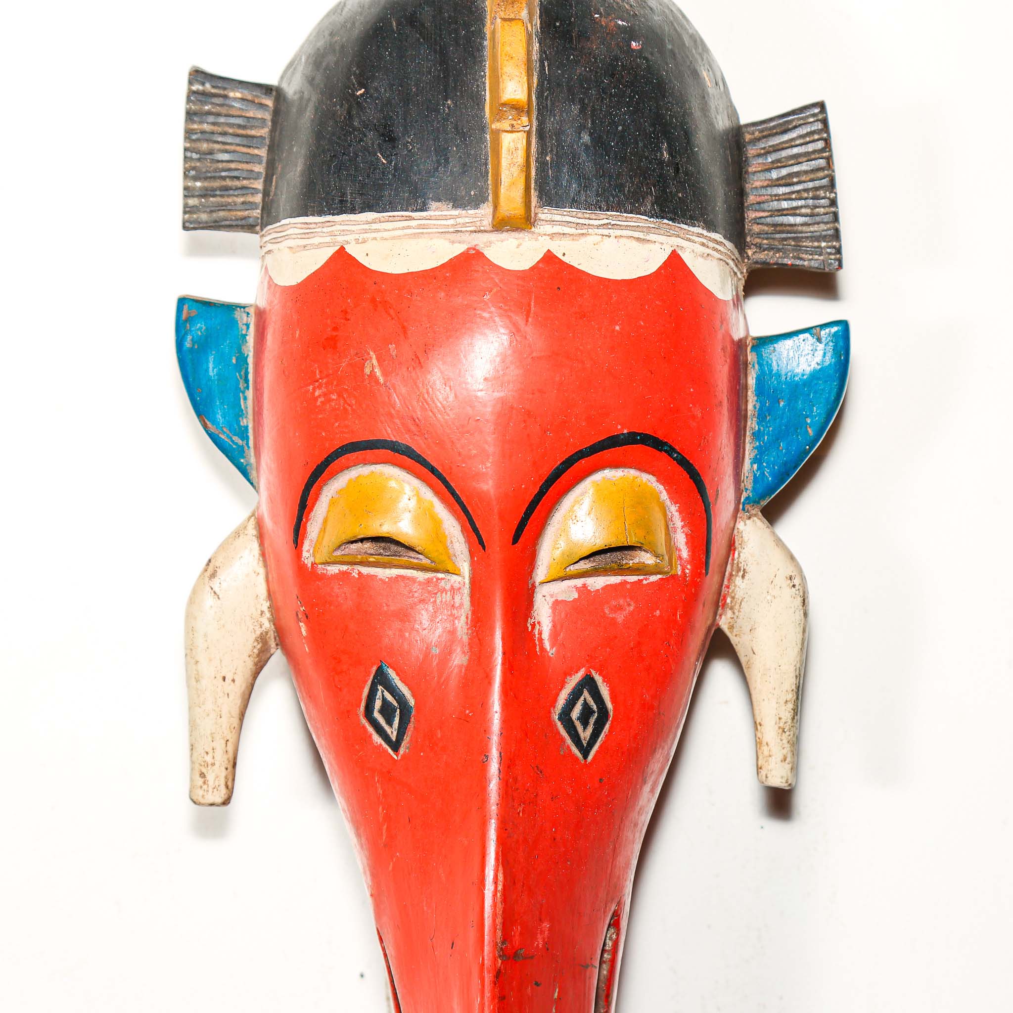 Colorful wooden mask with red face, blue ears, and yellow accents on a white background