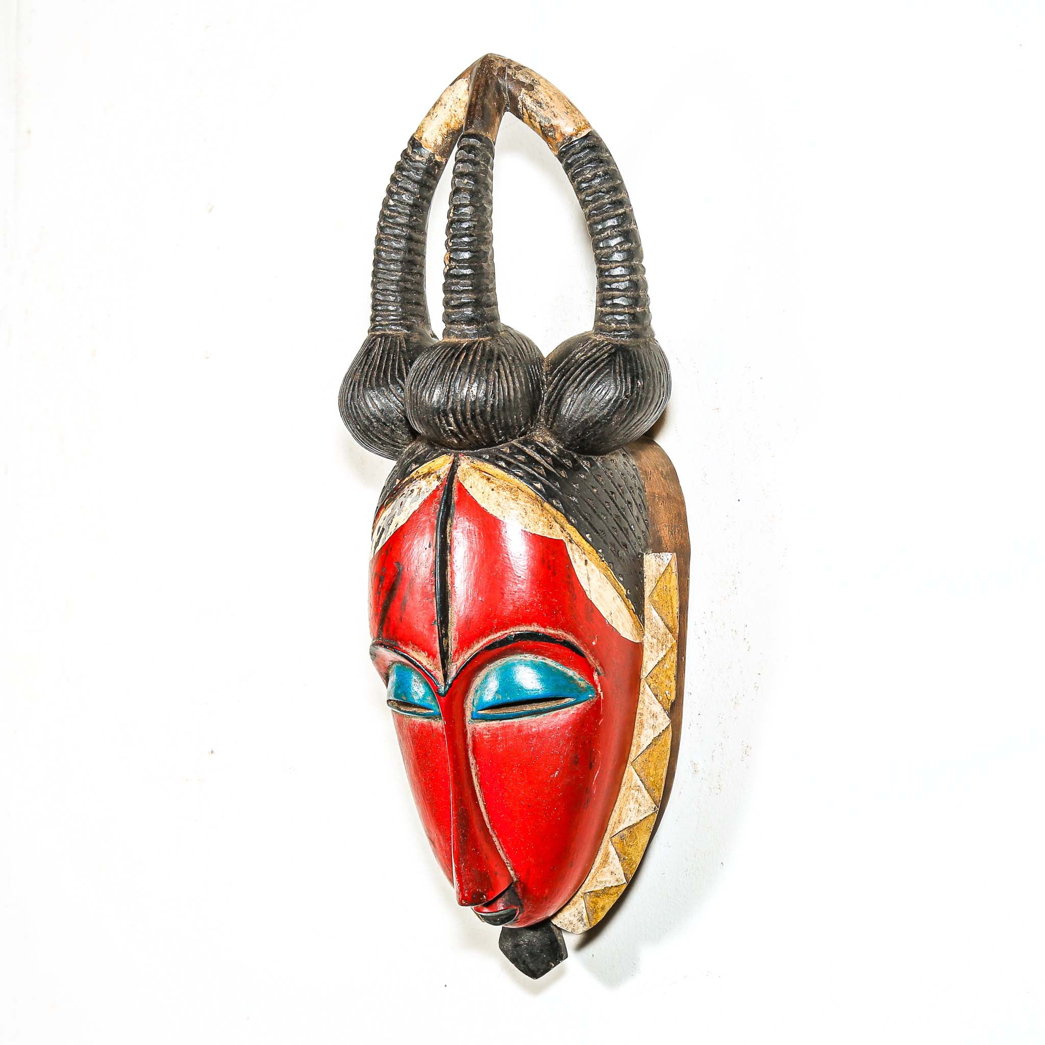African-style mask with red face, blue eyes, and decorative horns on a white background
