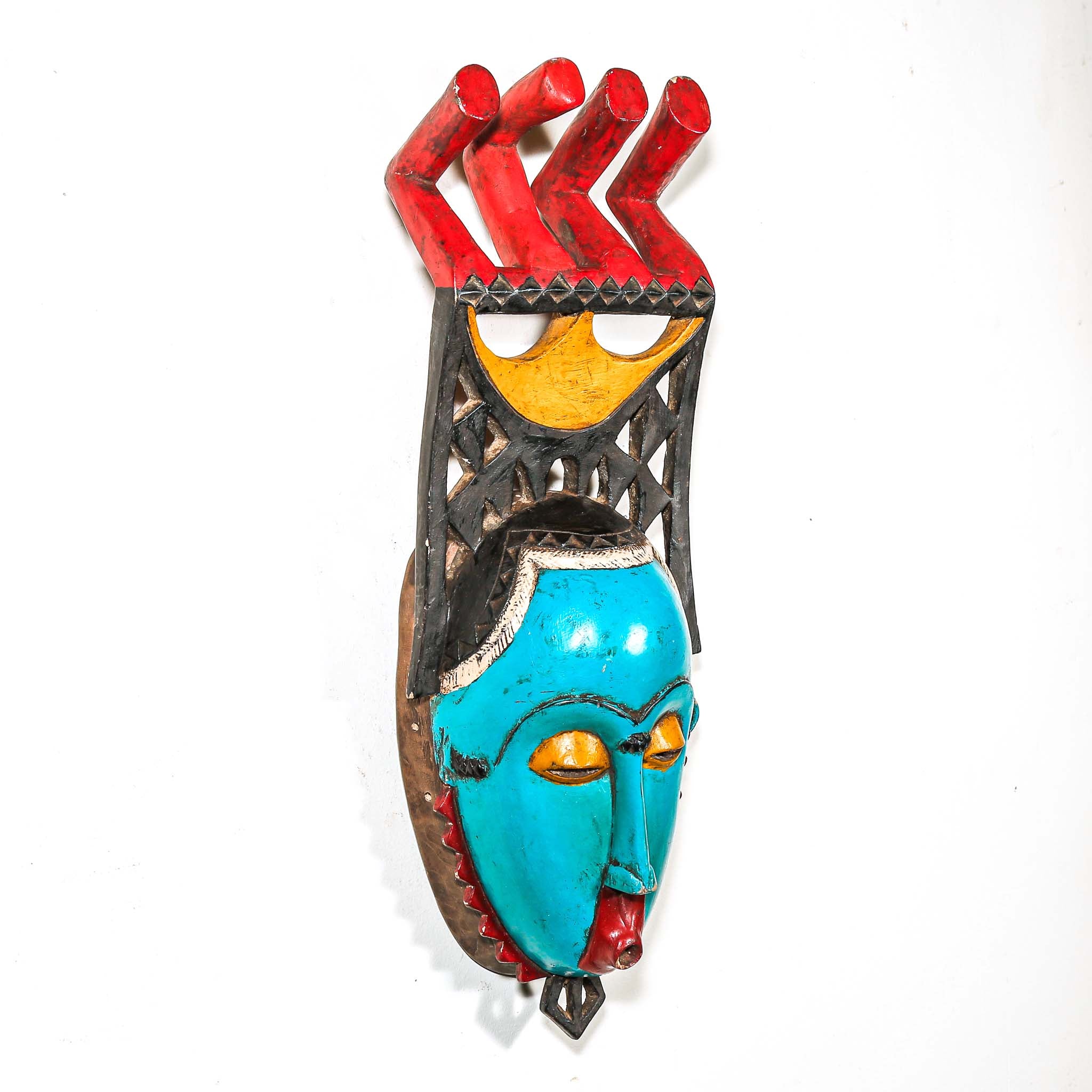 Colorful African wall mask with turquoise face, red and yellow accents on a white background