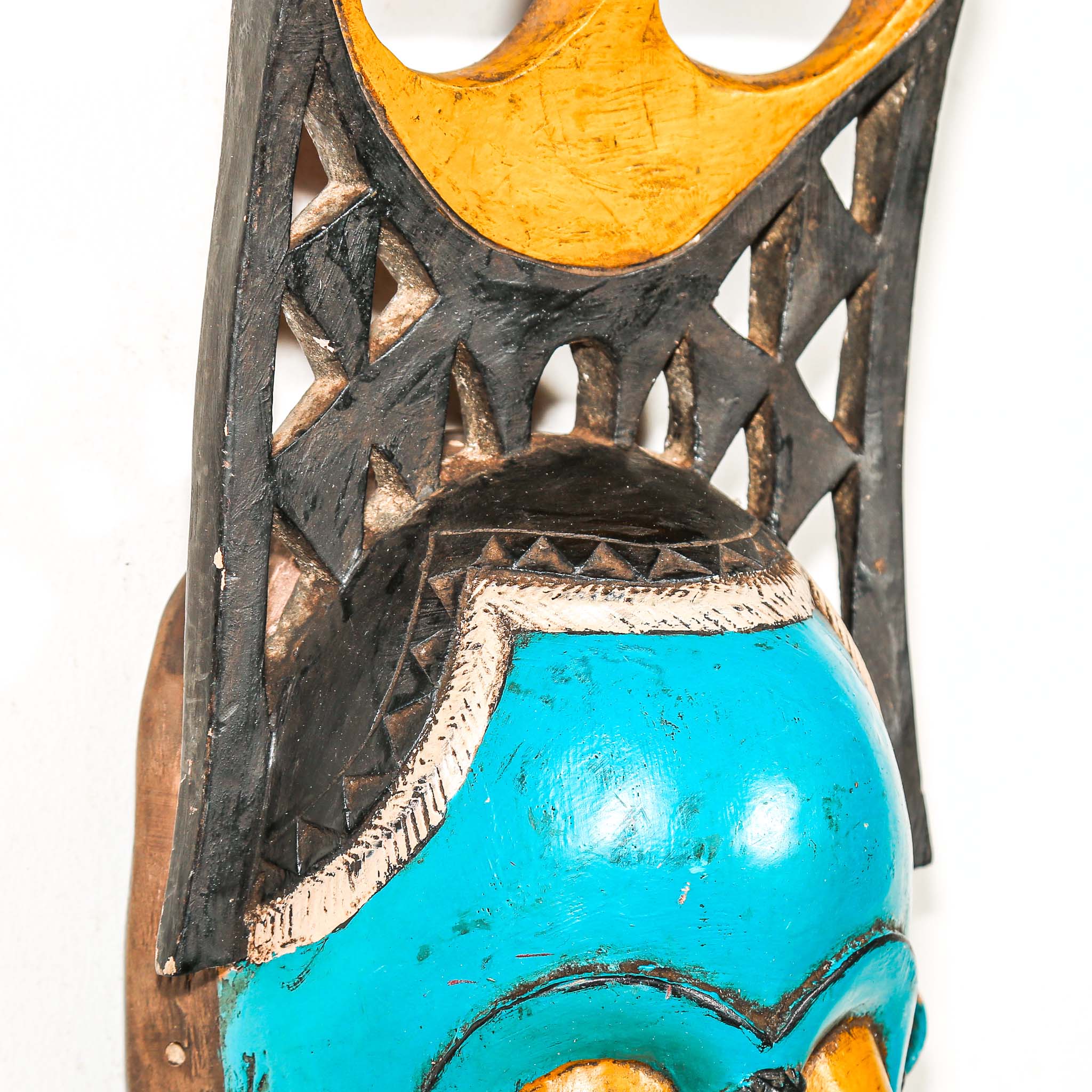 Colorful African wall mask with turquoise face, red and yellow accents on a white background