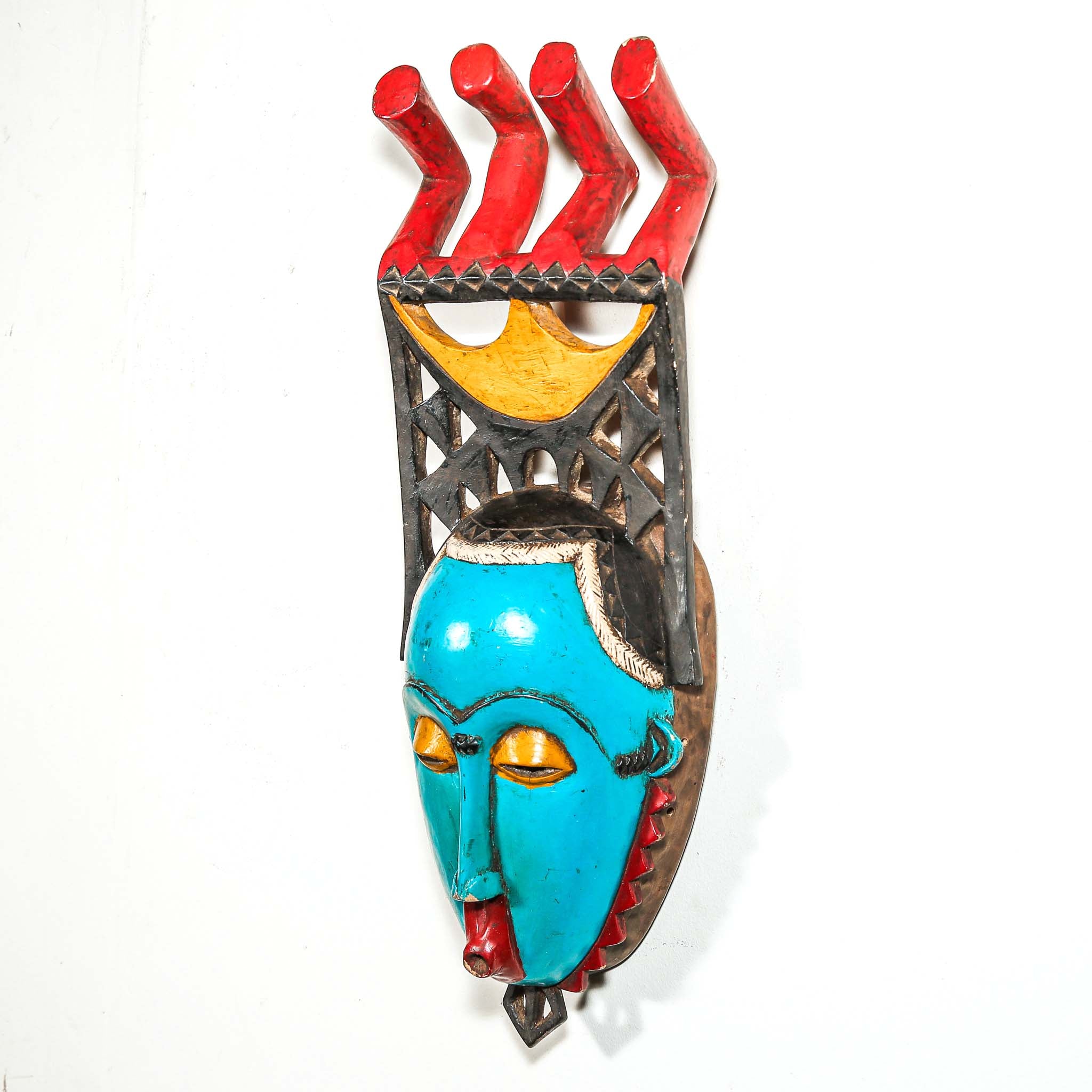 Colorful African wall mask with turquoise face, red and yellow accents on a white background