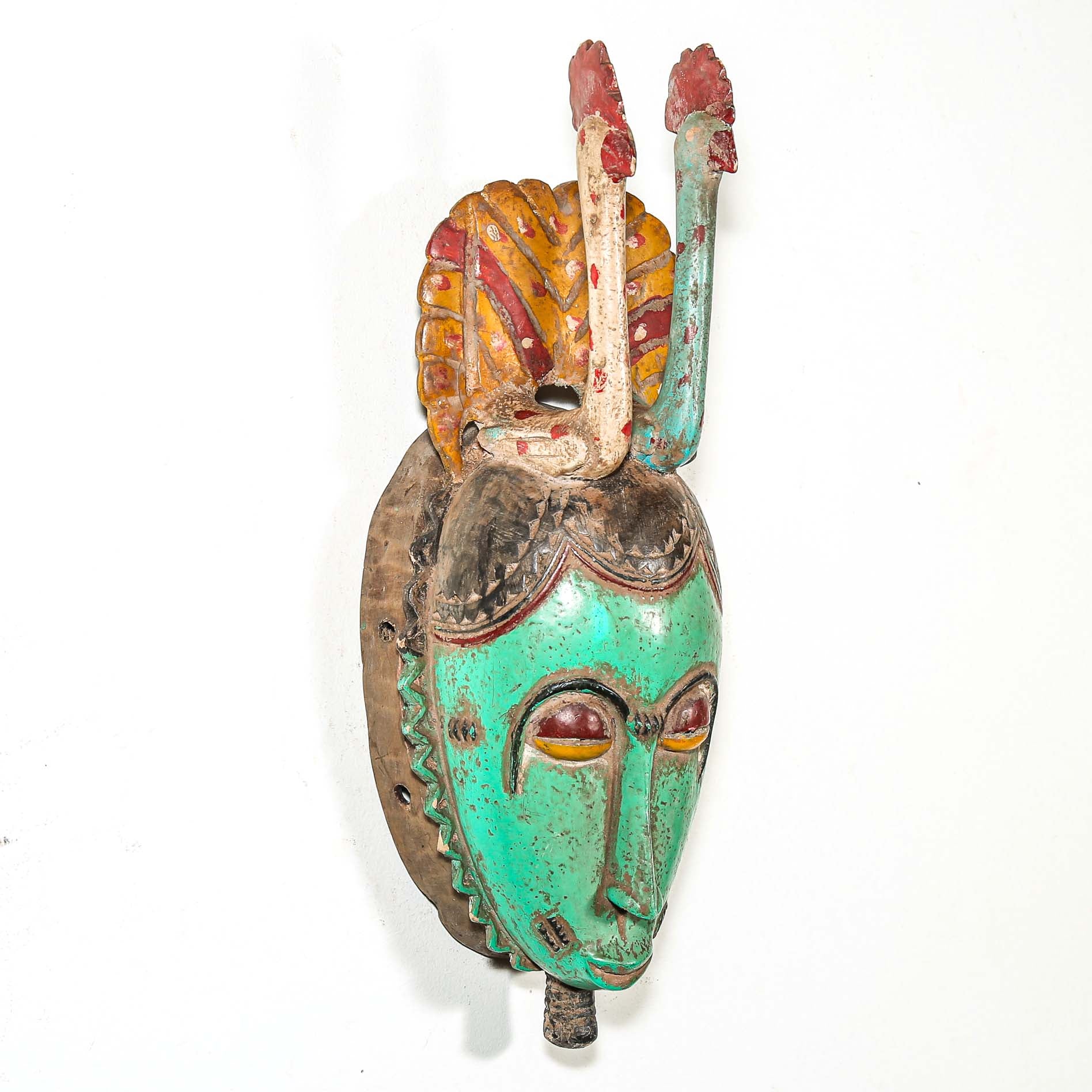 Tribal African mask with green face and colorful headdress with two birds on a white background