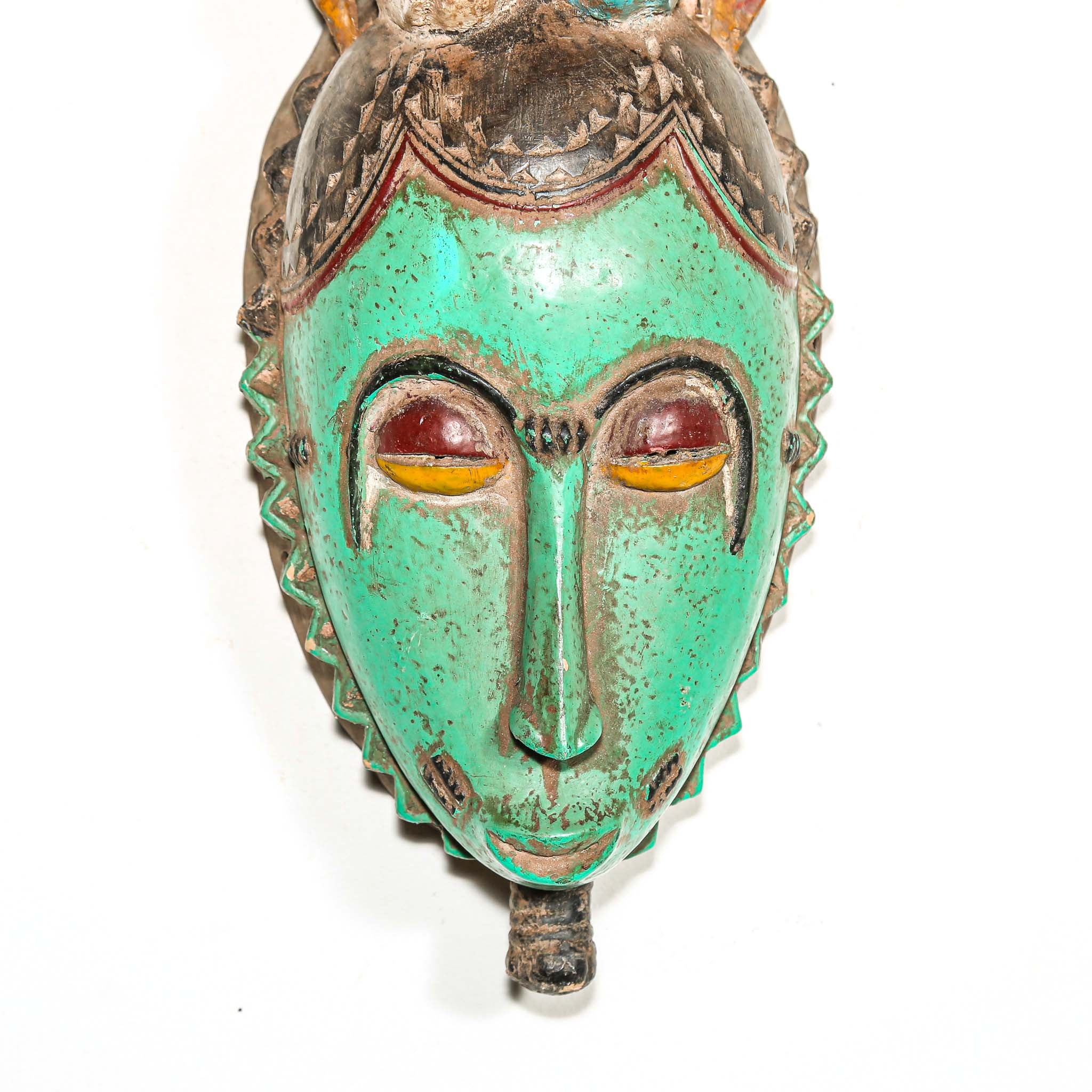 Tribal African mask with green face and colorful headdress with two birds on a white background