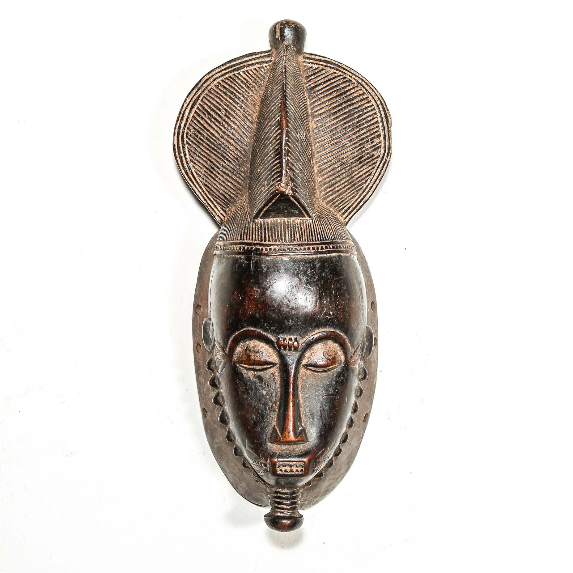 African black art mask made from wood with elaborate hair style hanging on a white wall