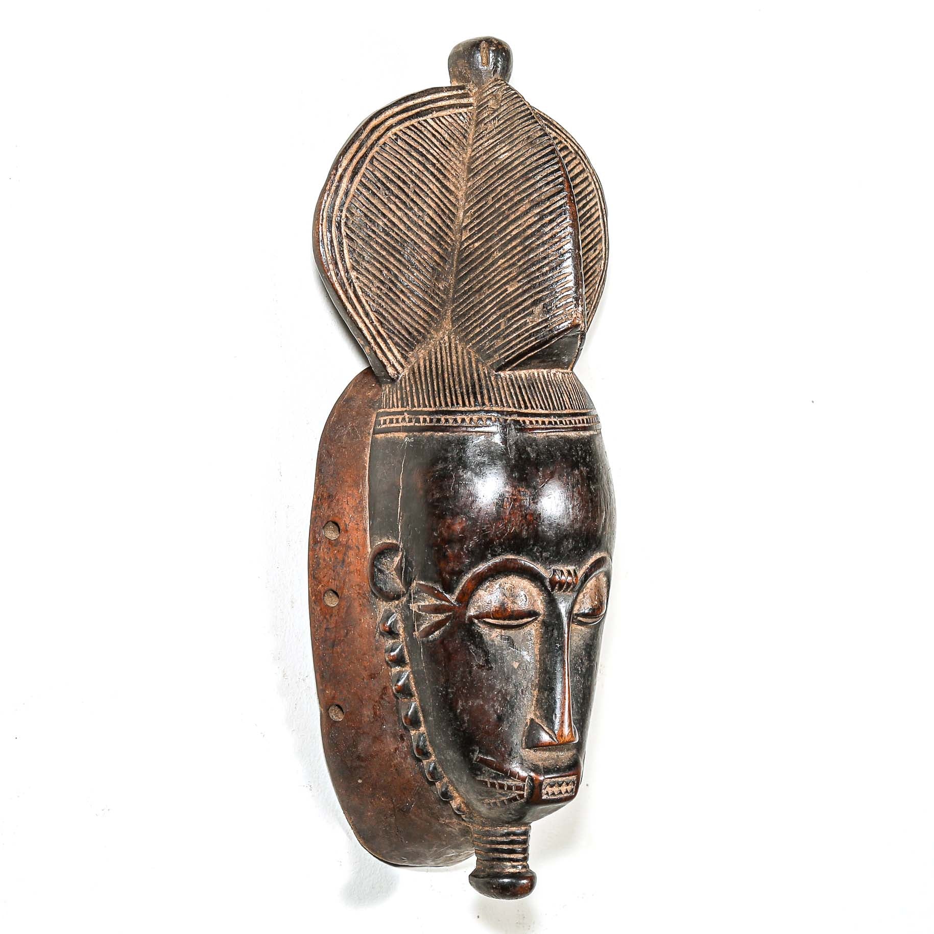 African black art mask made from wood with elaborate hair style hanging on a white wall