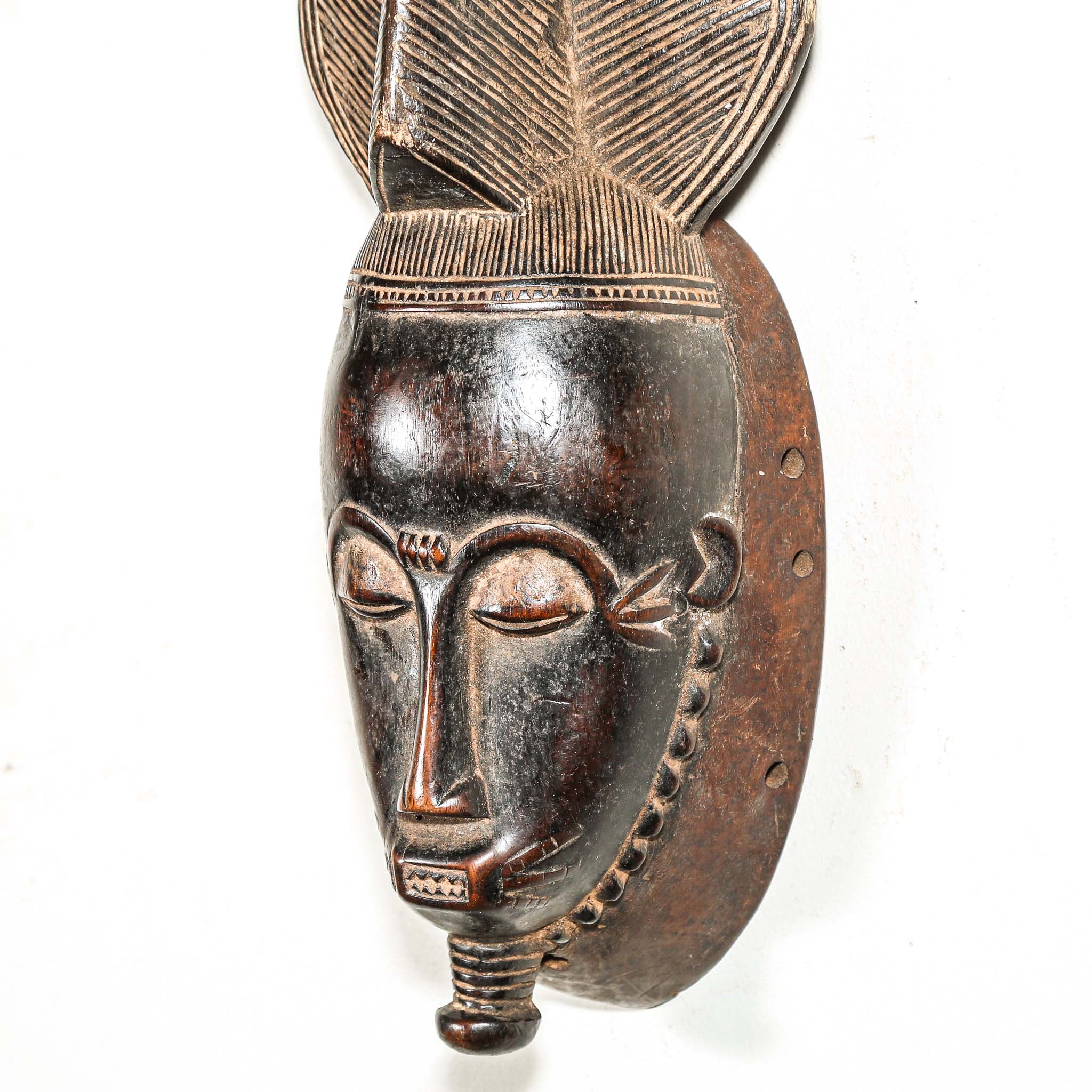 African black art mask made from wood with elaborate hair style hanging on a white wall