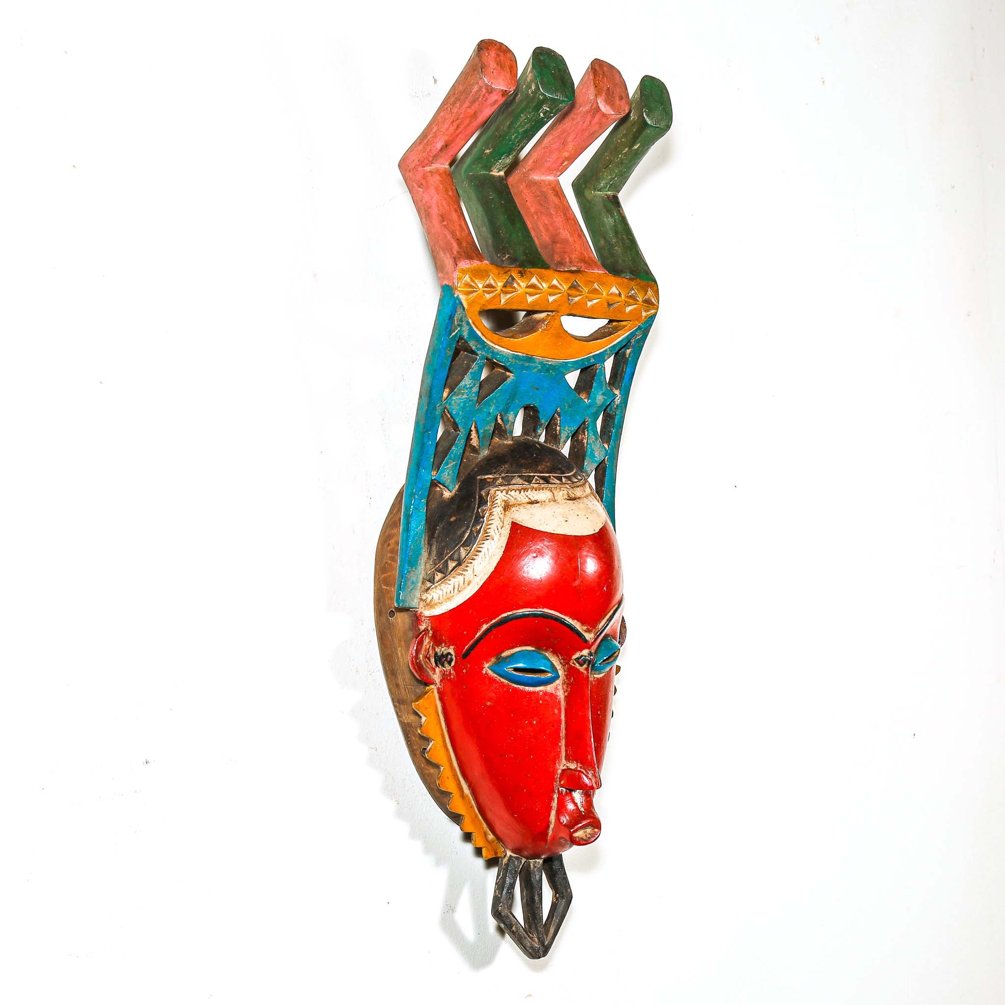 authentic tribal ceremonial red mask from Africa with colorful aesthetic displayed on a white wall