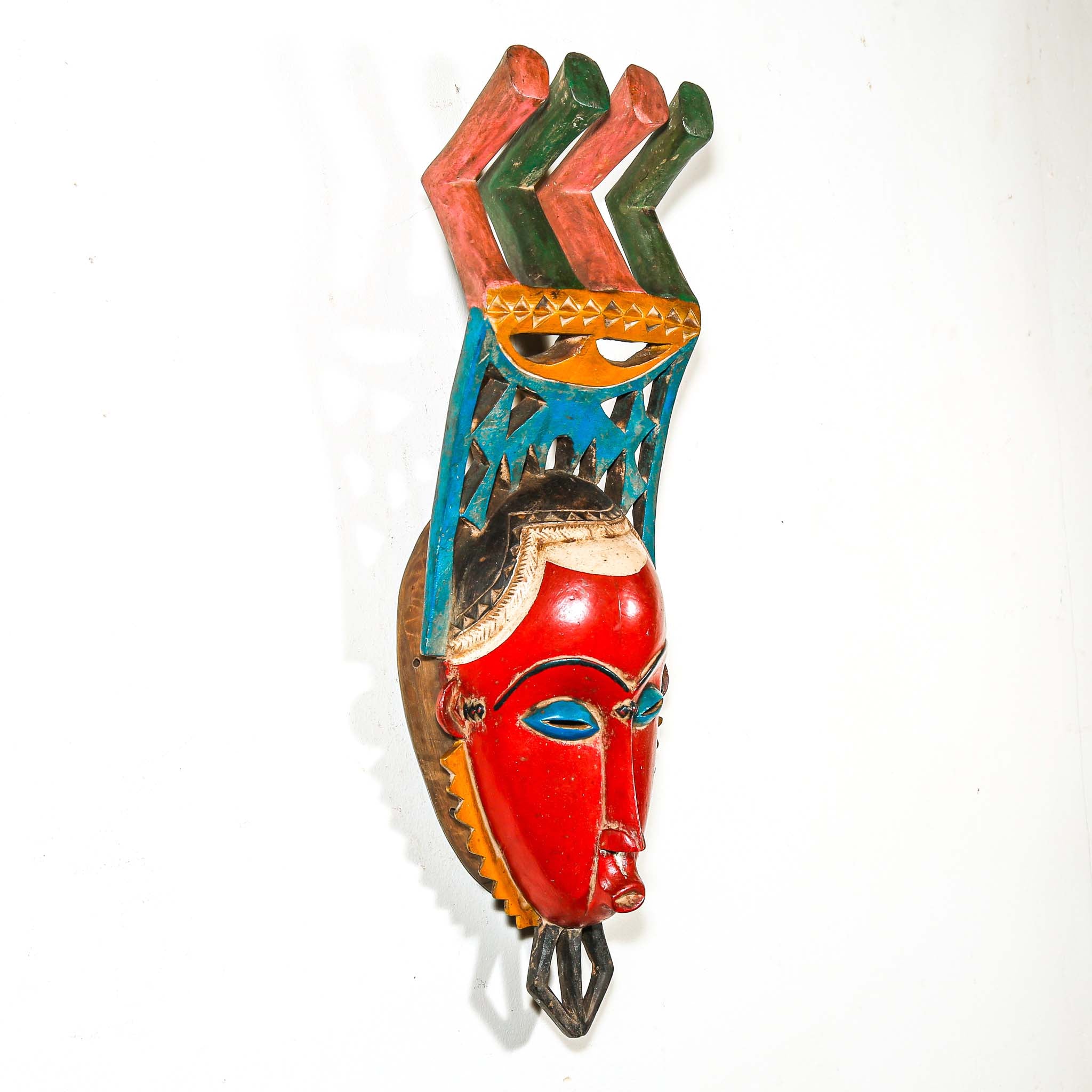 authentic tribal ceremonial red mask from Africa with colorful aesthetic displayed on a white wall