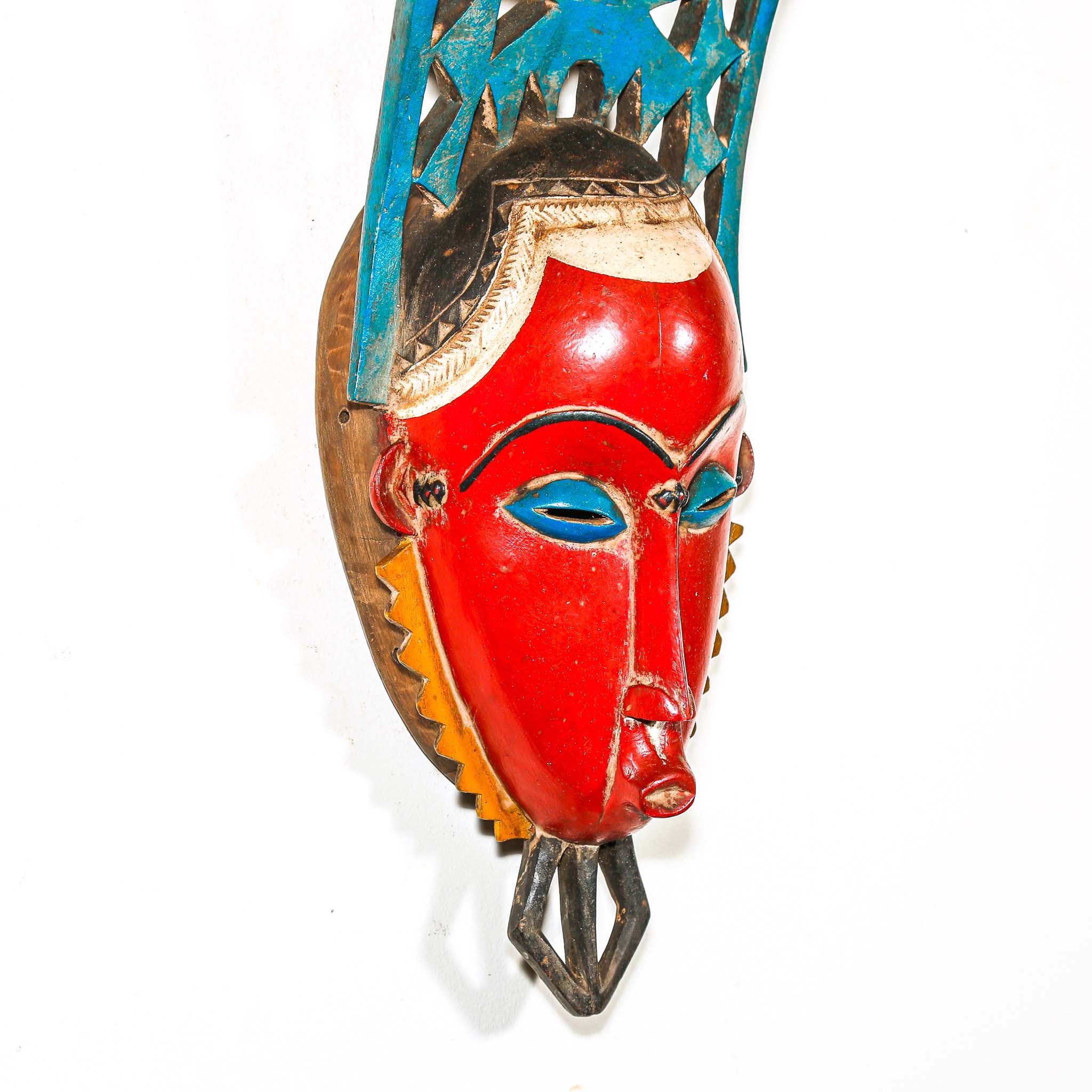 authentic tribal ceremonial red mask from Africa with colorful aesthetic displayed on a white wall