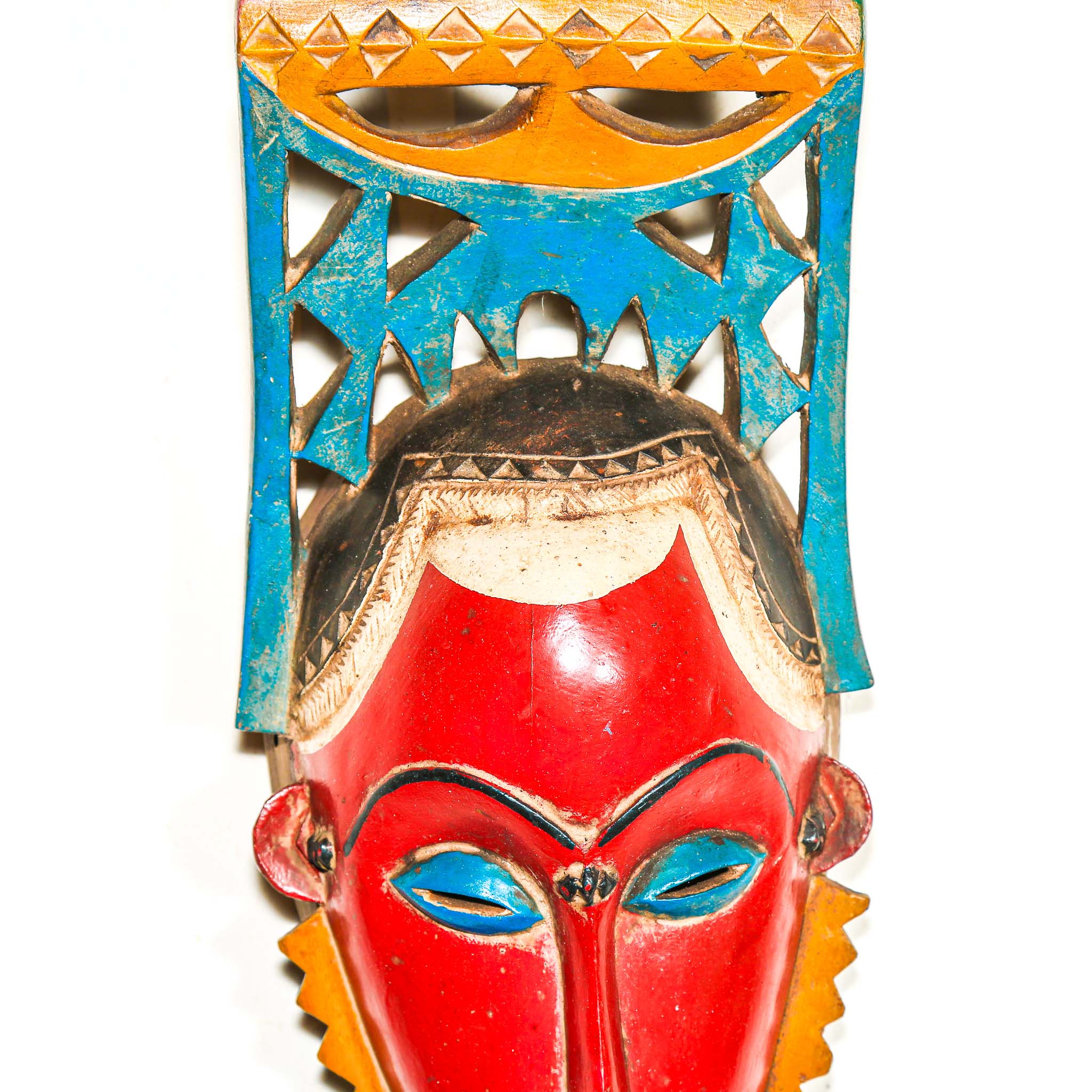 authentic tribal ceremonial red mask from Africa with colorful aesthetic displayed on a white wall