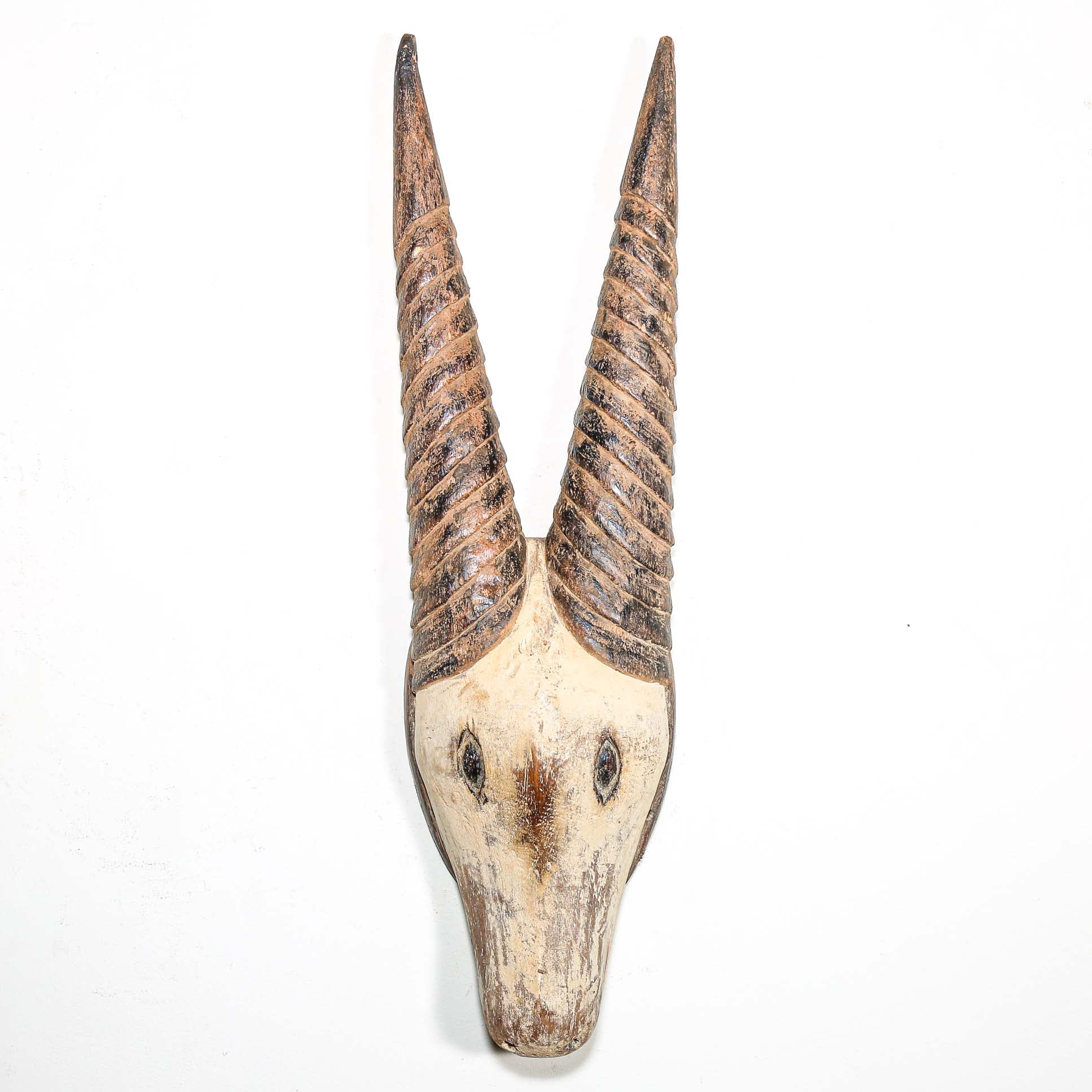 African mask in the shape of an antelope hanging on a white wall