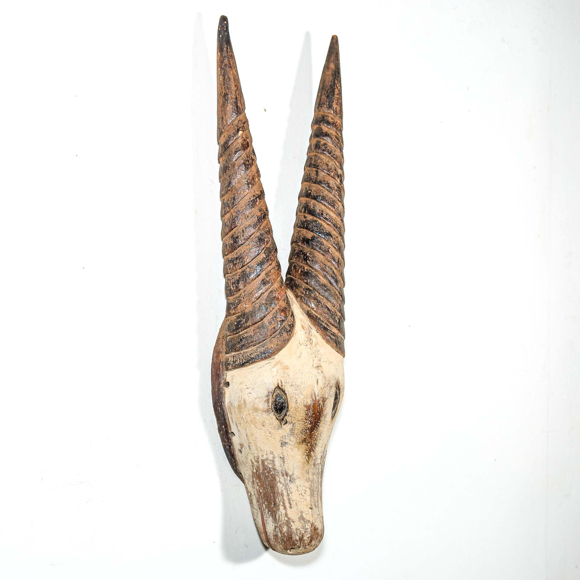 African mask in the shape of an antelope hanging on a white wall