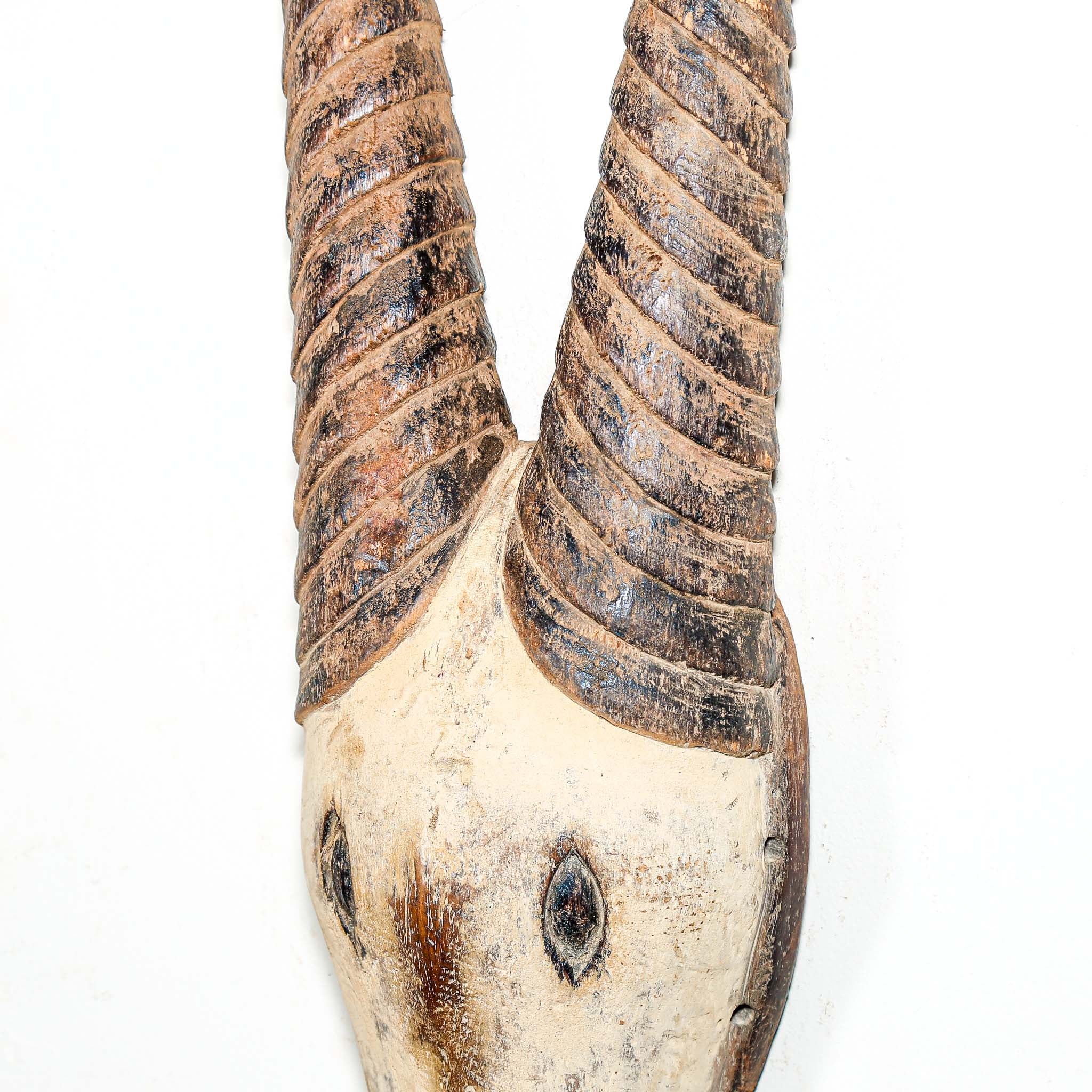 African mask in the shape of an antelope hanging on a white wall
