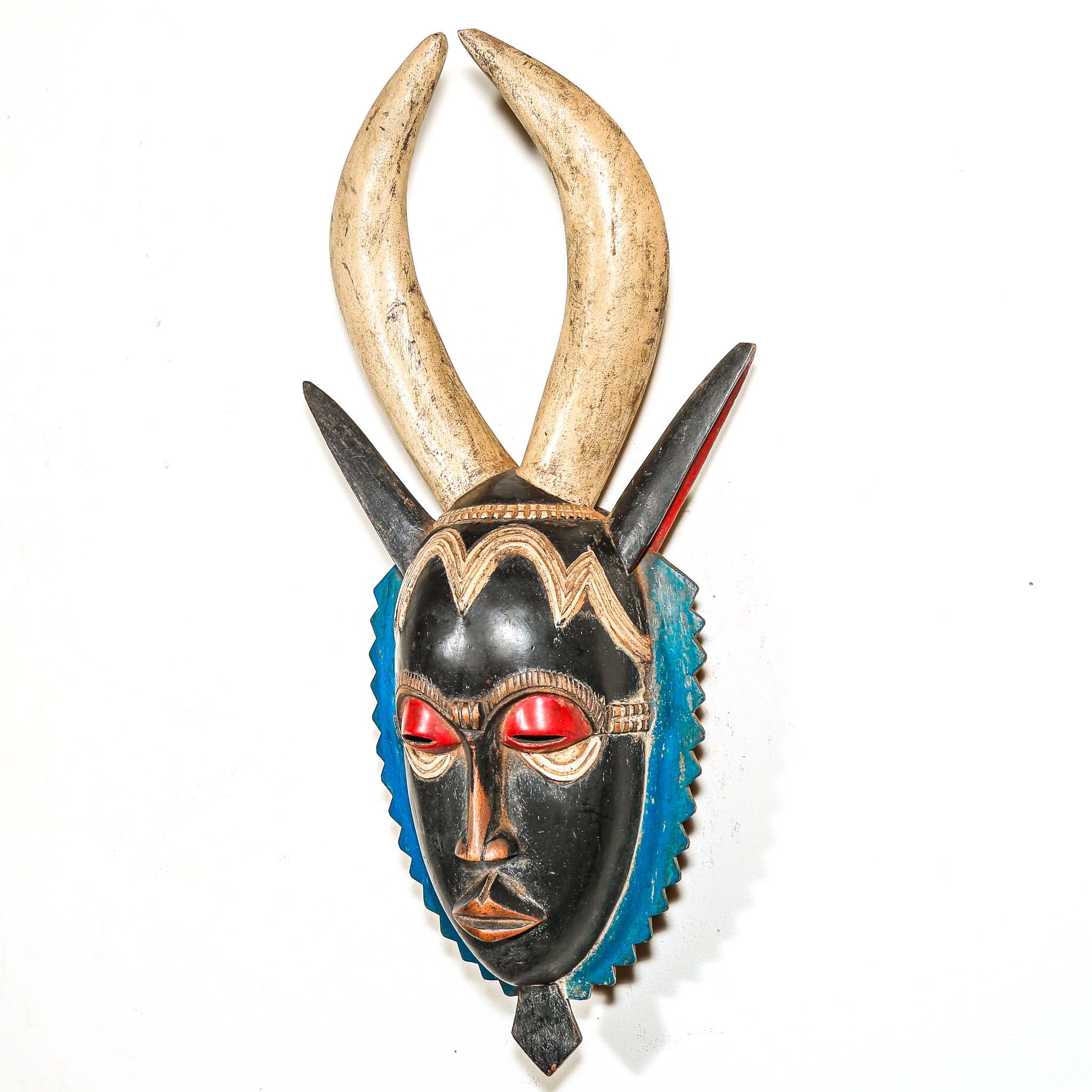 A vintage colorful African wood mask with large horns and a black face on a white background