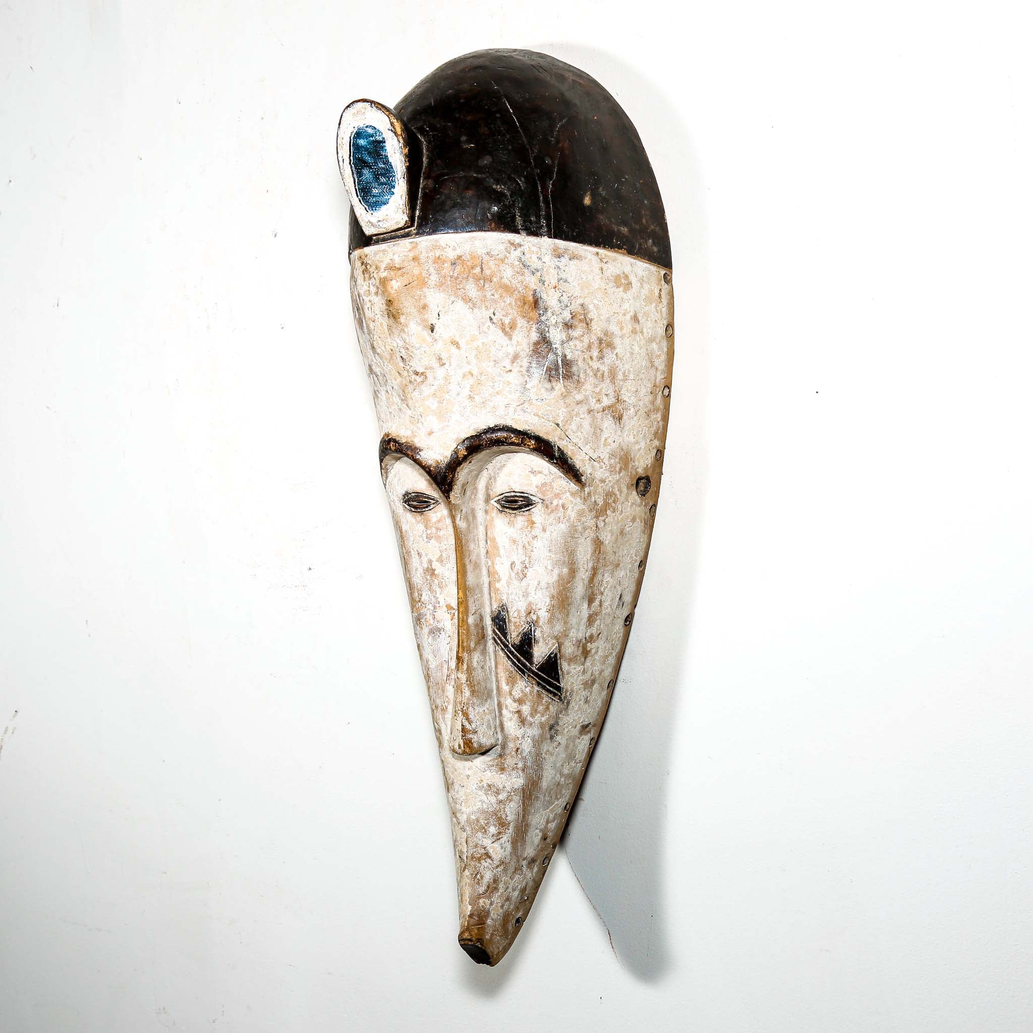 Authentic African mask to purchase online with neutral color designs hanging on a white wall