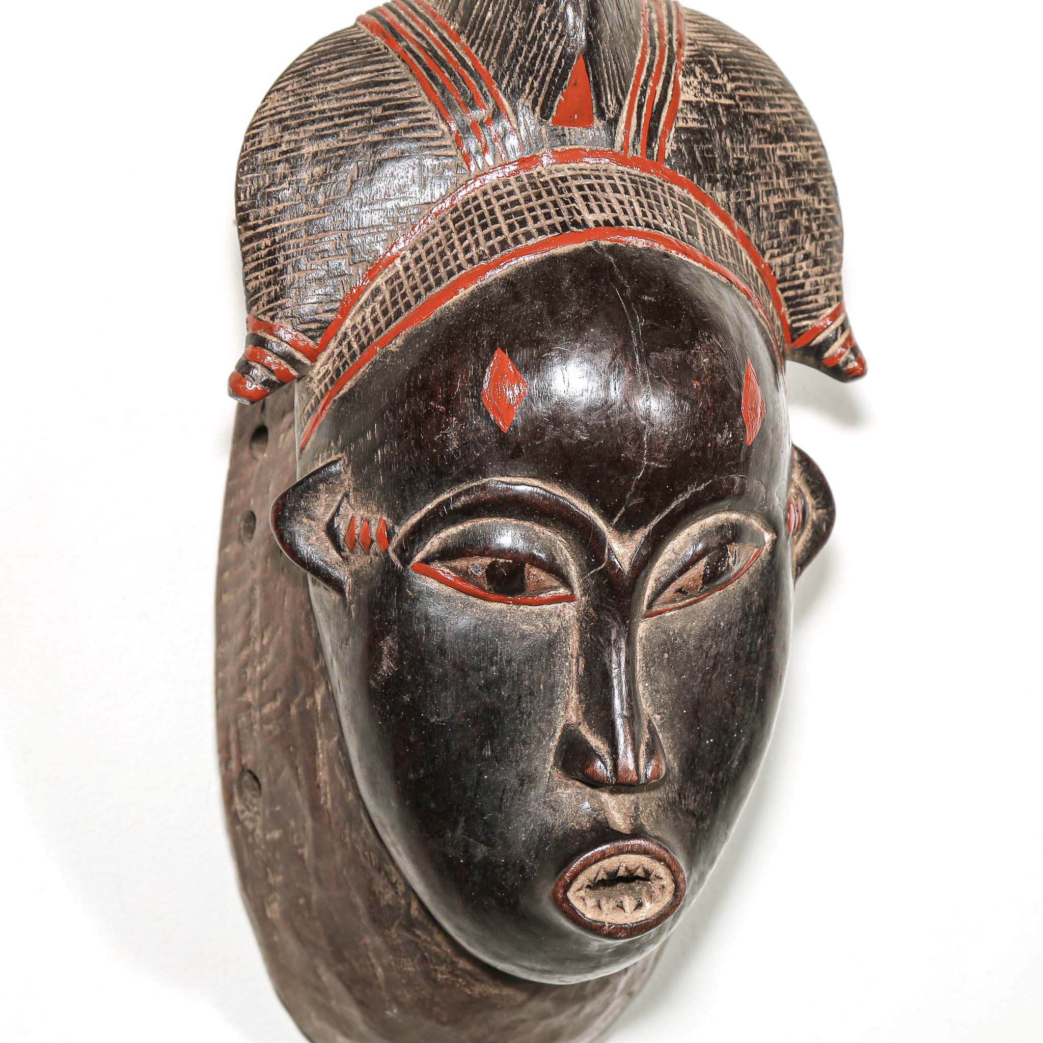 Wooden traditional African mask with black art face and red accents on a white background