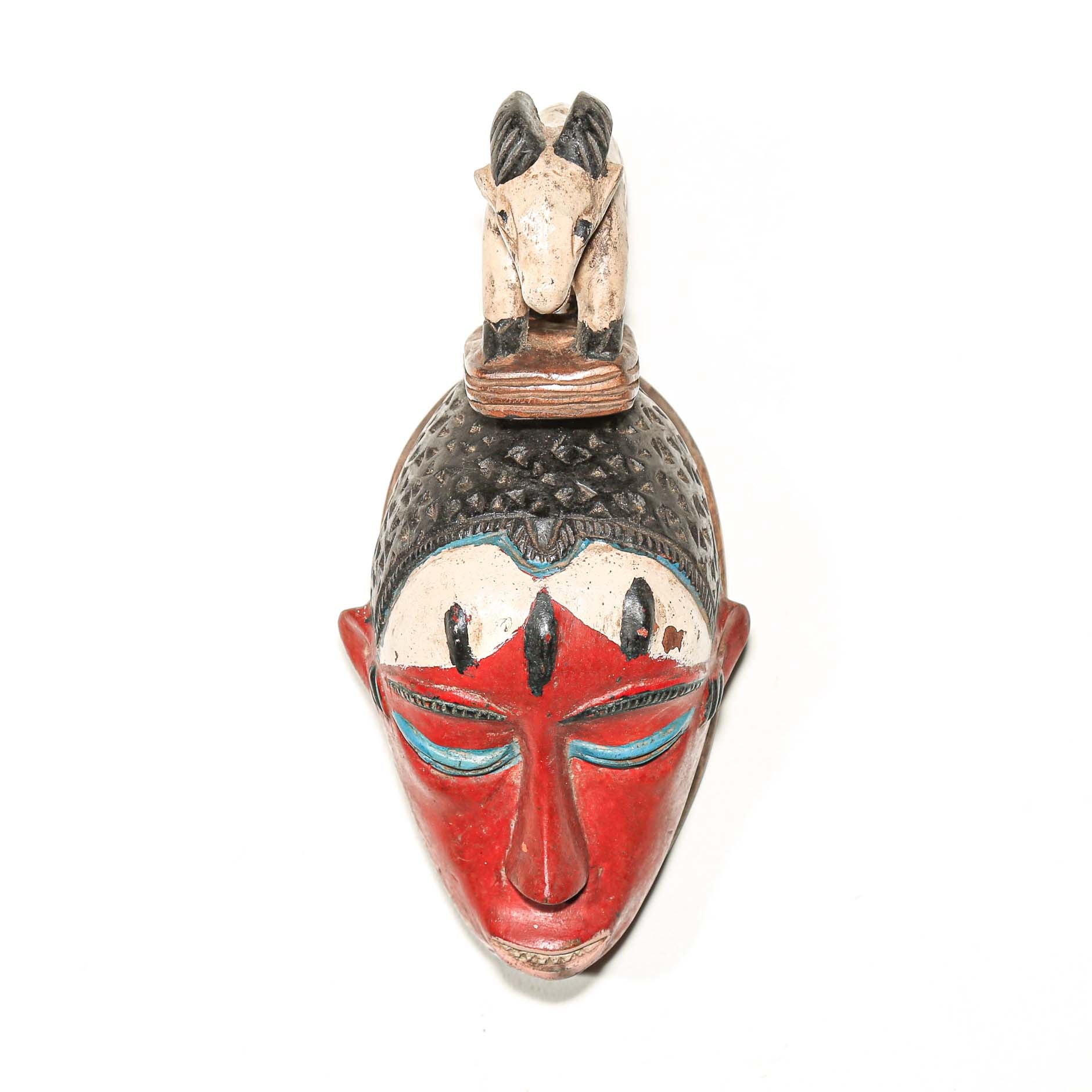 Colorful Decorative African mask with a small animal figure on top hanging on a white wall