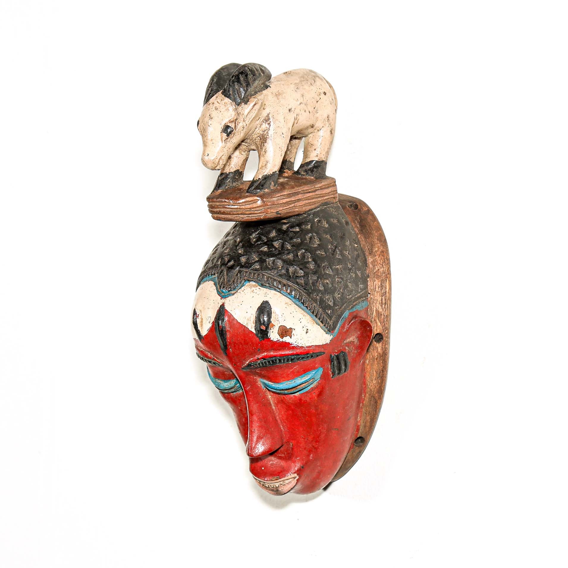 Decorative African mask with a small animal figure on top hanging on a white wall