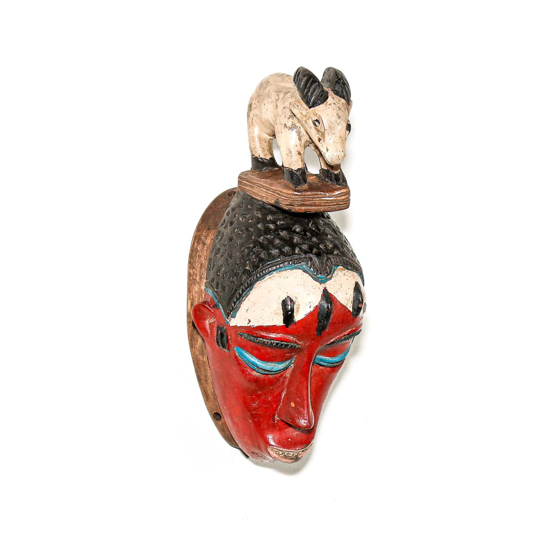 Colorful Decorative African mask with a small animal figure on top hanging on a white wall