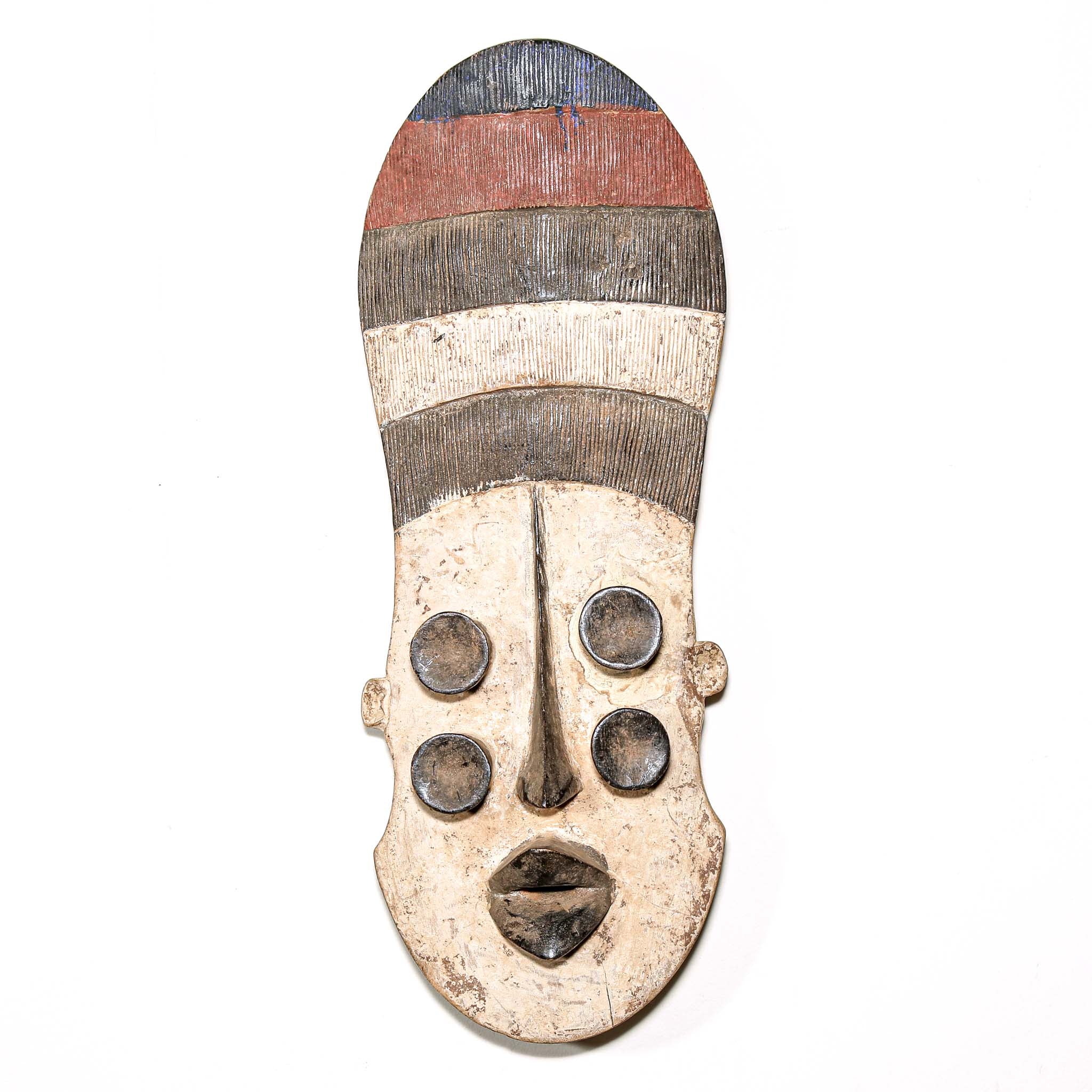 Wooden mask from Africa with striped patterns and four eyes on a white wall