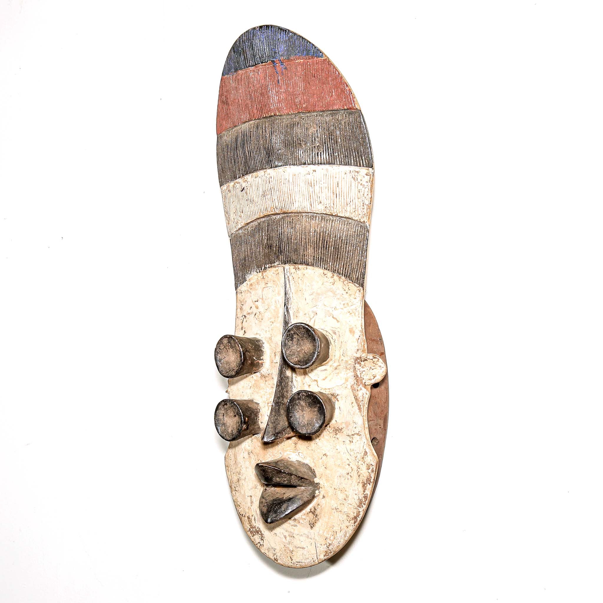 Wooden mask from Africa with striped patterns and four eyes on a white wall
