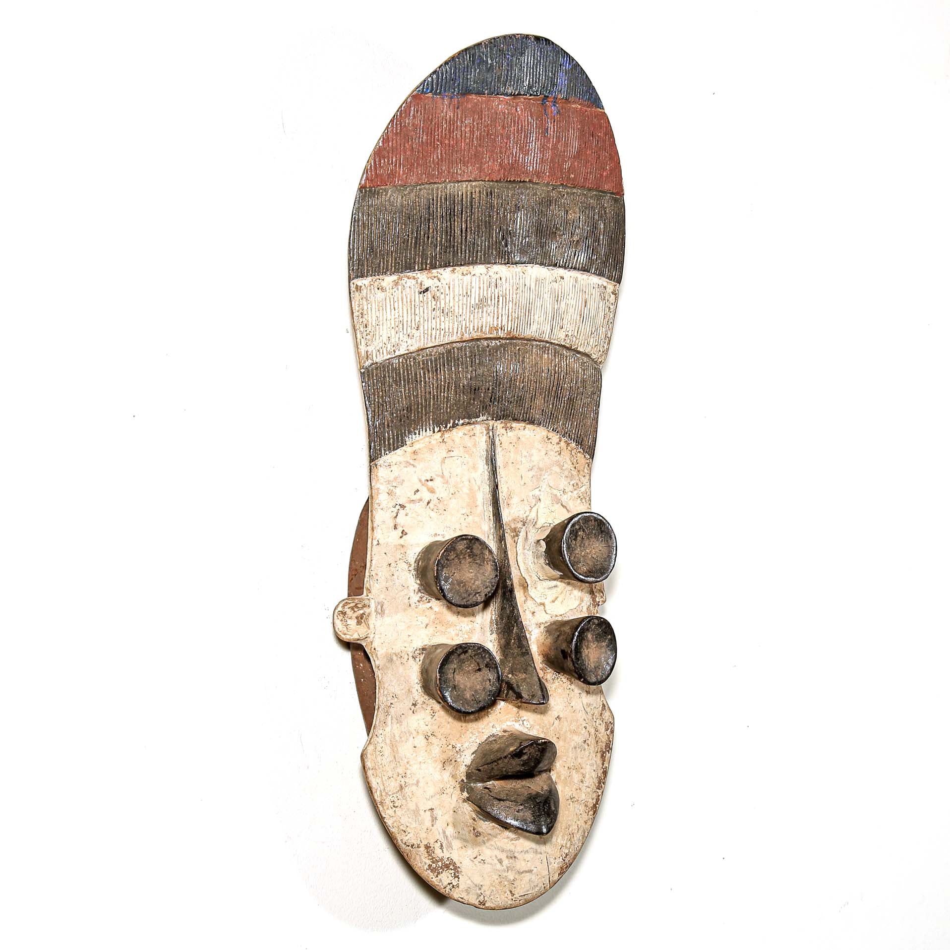 Wooden mask from Africa with striped patterns and four eyes on a white wall