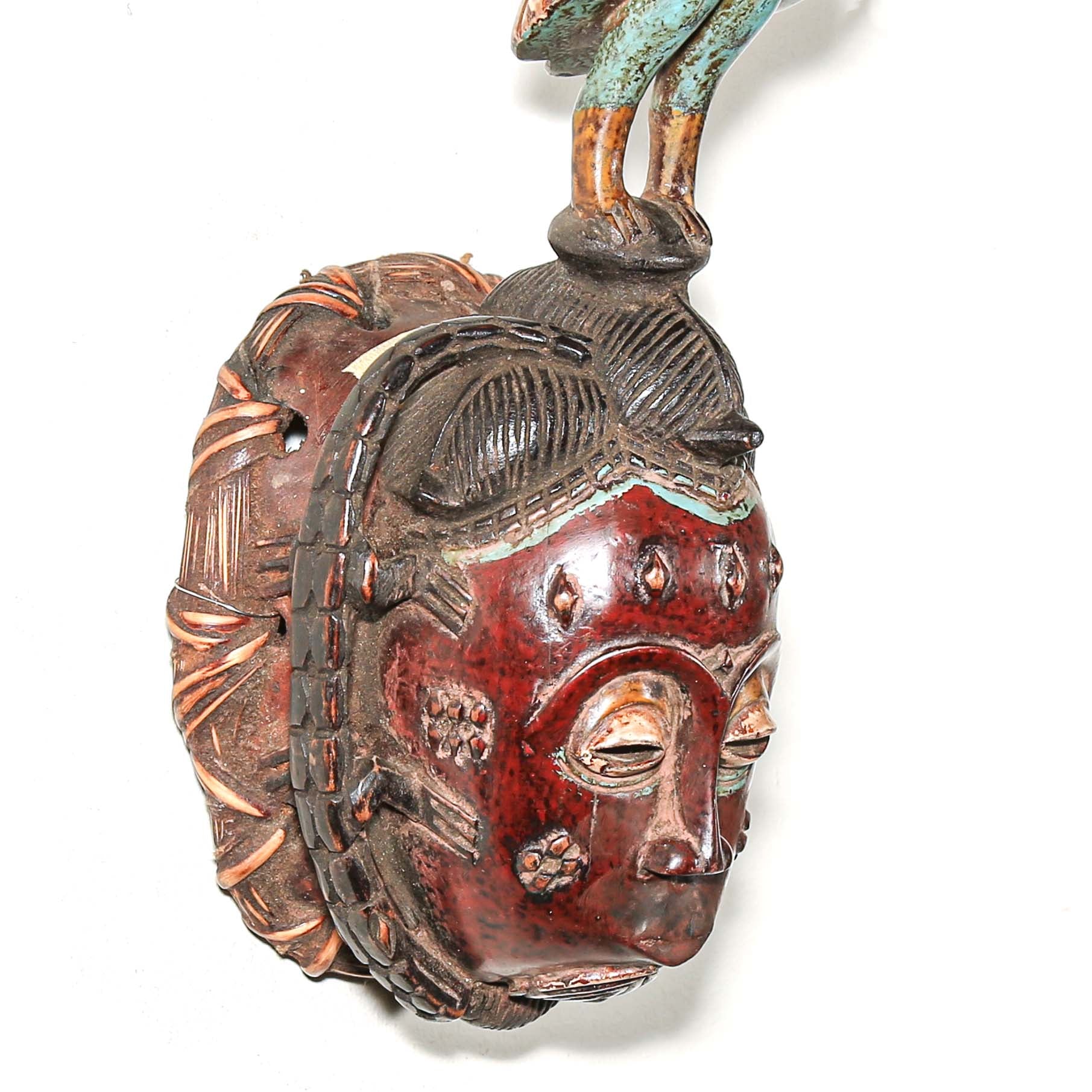 Guro African mask with colorful bird headdress. Red blue brown and black colors hanging on the wall